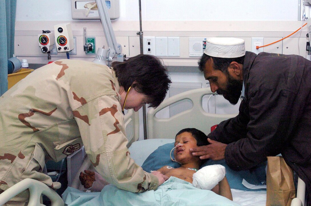 Maj. Teresa Paris, a physician assistant, examines 8-year-old Orphan while his father comforts him in the Craig Joint Theater Hospital in Bagram Air Base, Afghanistan. Orphan lost his right leg and most of the flesh on his left leg when he stepped on a mine planted by Taliban forces near his home. (U.S. Air Force photo/Staff Sgt. Thomas J. Doscher)