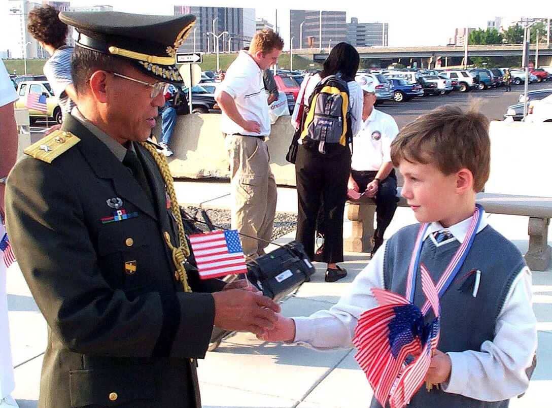 William P. Scaring, 7, presents Philippine  Army Brig. Gen. Delfin N. Lorenzana an American flag as the  general heads for DoD's first anniversary ceremony of the  terrorist attack on the Pentagon Sept. 11, 2002. Lorenzana,  Philippine defense attache in Washington, said the attack  united the whole world to fight against the terrorists.  Photo by Rudi Williams.