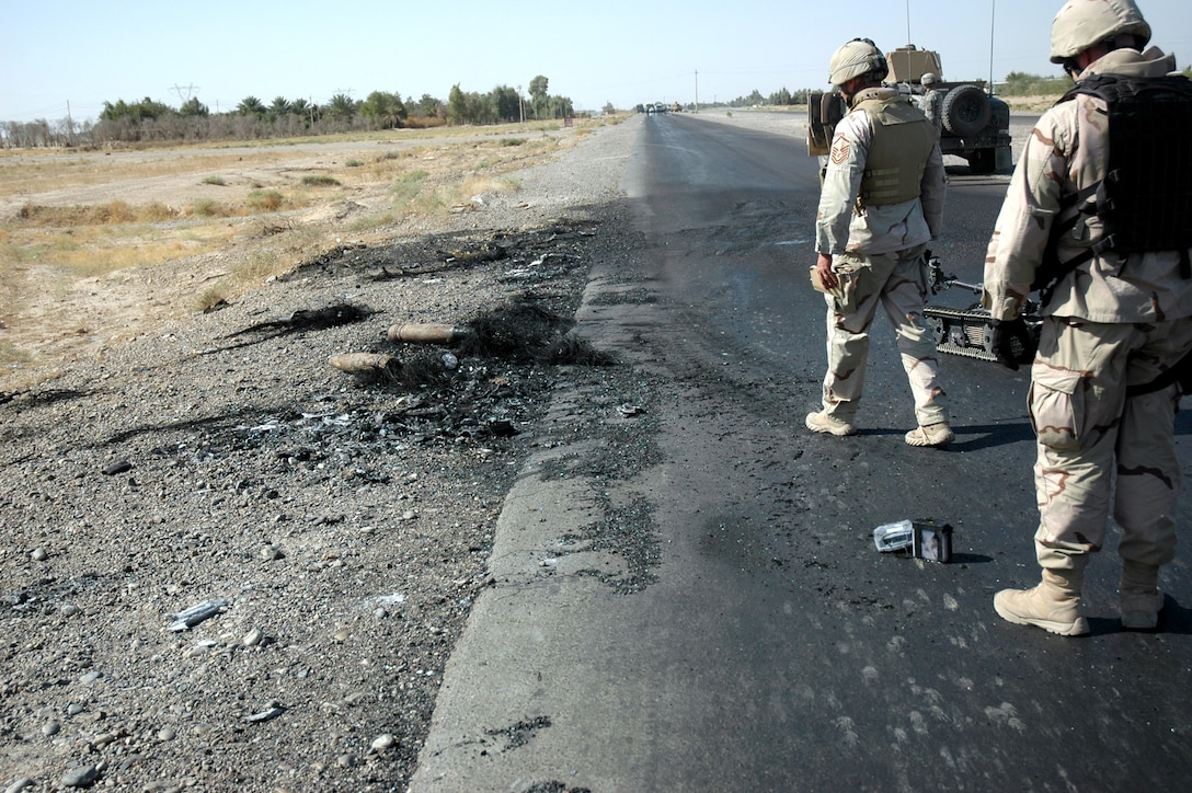 Waiting for Explosive Ordnance Disposal to confirm the scene is safe, Staff Sgt. Christopher Hawks (front left) and Master Sgt. Albert Schneider (front right), prepares to collect evidence and obtain pictures in Paliwoda, Iraq. The EOD team from Paliwoda and Sergeant Schneider's Weapons Intelligence Team had just arrived at the scene of two improvised explosive devices detonations targeting civilian vehicles on Main Supply Route Tampa. (U.S. Air Force photo) 
