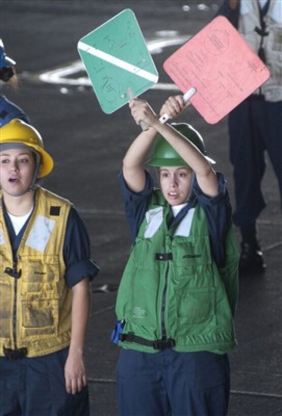 U.S. Navy Seamen Angie Jimenez (right) signals from the hanger bay of the USS Ronald Reagan (CVN 76) to her counterpart on board the USNS Flint (T-AE 32) during an off-load of ammunition as the ships operate in the Western Pacific Ocean on April 6, 2007.  The Reagan off-loaded thousands of pounds of ammunition and bombs to the Flint during a three-day ammo offload evolution.   The Ronald Reagan Carrier Strike Group is deployed in support of U.S. military operations in the Western Pacific.  