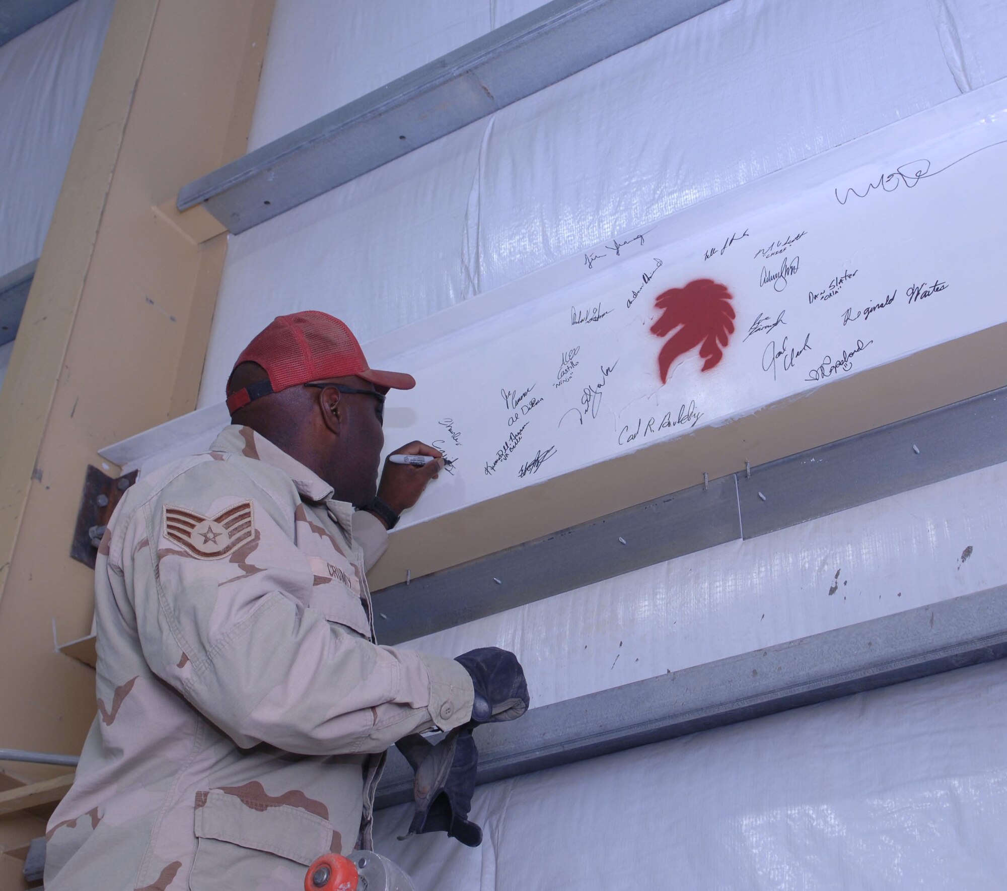 Staff Sgt. Charles Crumity, a heavy equipment operator for the 1st Expeditionary RED HORSE Group, places his signature on a beam to signify the completion of the building. The building is the first permanent structure for customs at Bagram Airfield. (U.S. Air Force photo/Staff Sgt. Kevin Tomko)