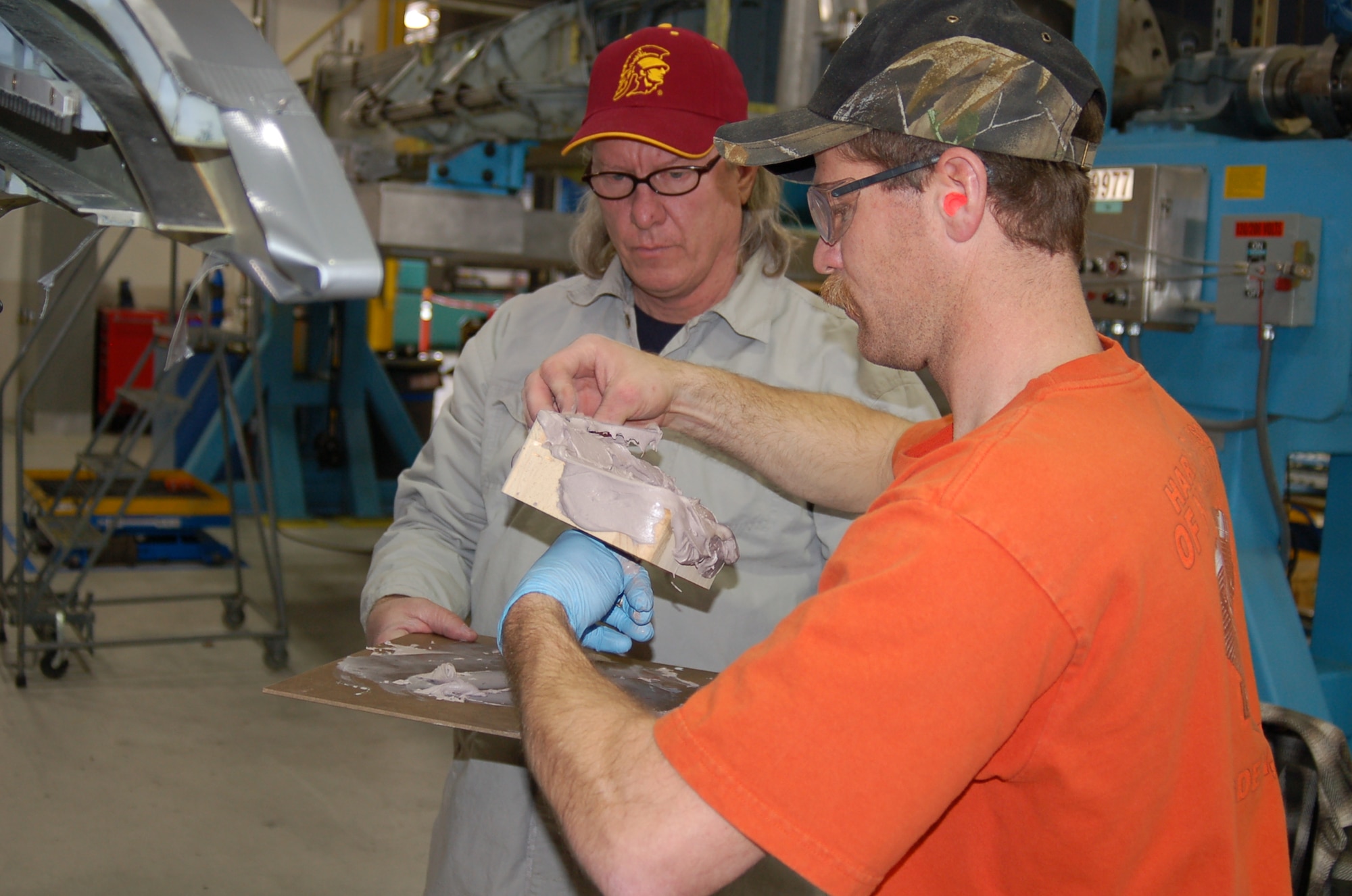 Assisted by Stan Martindale, facility work leader, Mr. Fowles applies the automotive body filler to a wooden block that will help form the splash mold. Photo by Bill Orndorff
