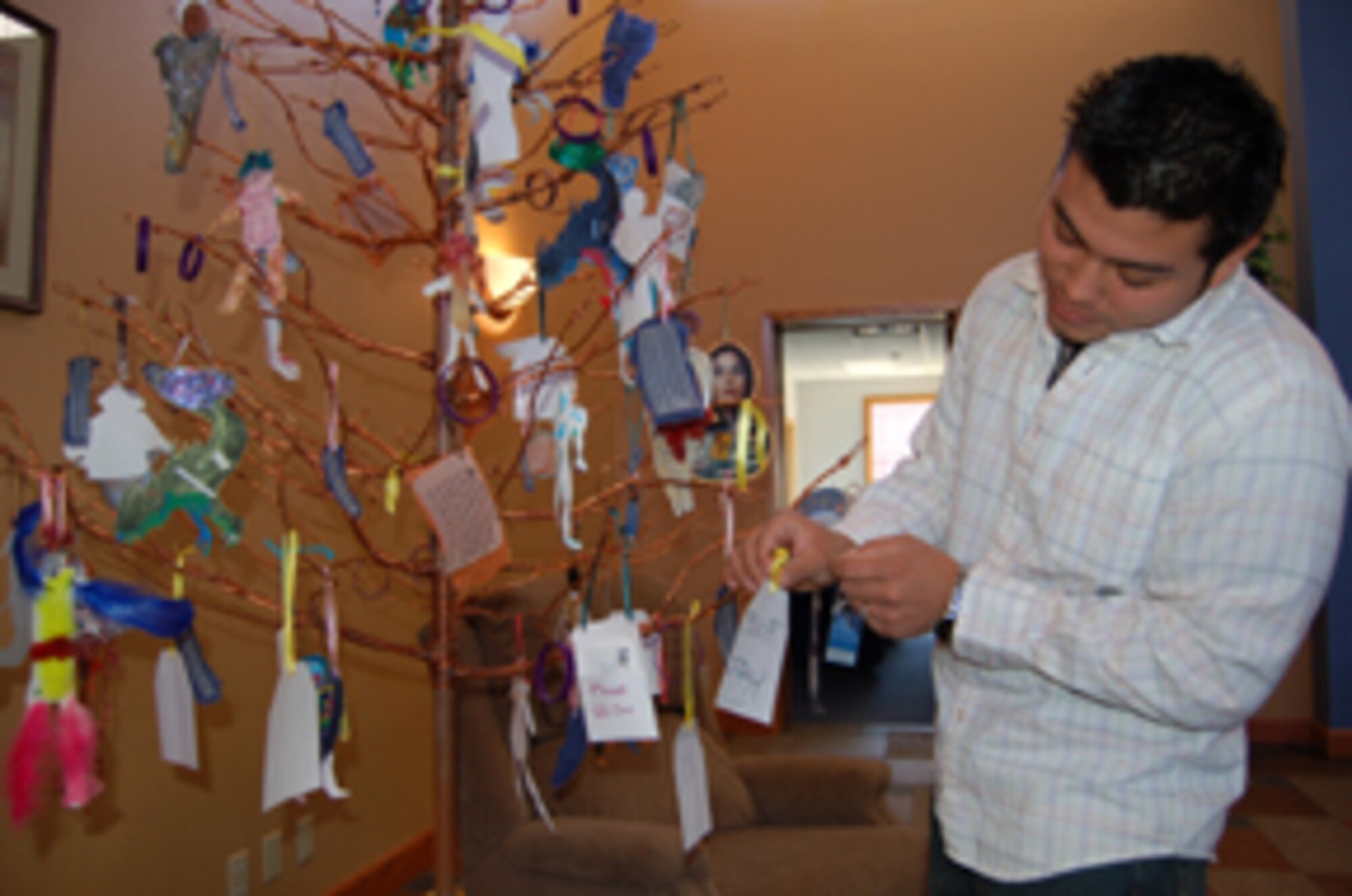 Senior Airman Edic Moreno, 319th Services Squadron, places a yellow ribbon with the name of his former supervisor, Tech. Sgt. Steven Fry, 319 SVS, who is currently deployed on the tree of integrity, strength and hope at the community activity center April 17 during the art expressions event sponsored by the base Sexual Assault Prevention and Response office. The event is to artistically express ideas and experiences take a stand and make a difference in creating a more caring and loving community for Sexual Assault Prevention Awareness Month.