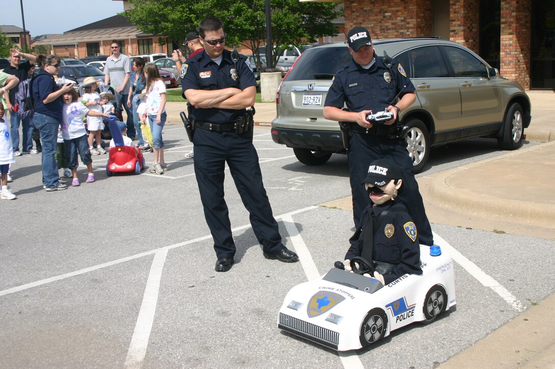 Wichita Falls Police Department Officers Jeff Hughes and Harold McClure demonstrate the abilities of Curtis E. Cop, a remote-controlled animatronic puppet, during the Child Development Center Month of the Military Child parade April 19. (U.S. Air Force photo/Staff Sgt. Tonnette Thompson)