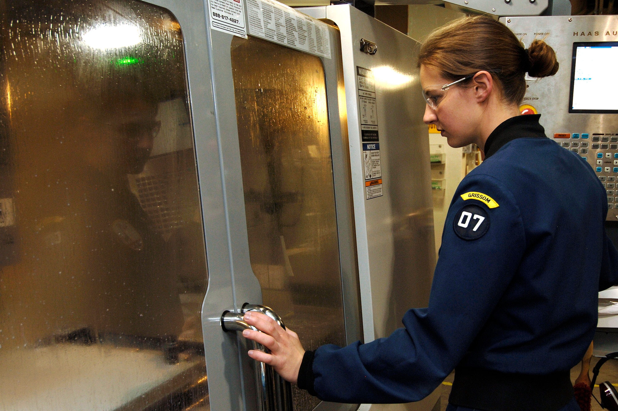 Cadet senior Katherine Gulczynski mills out a side panel April 12 for Falcon Satellite-5 using a Computer Numerical Control. computer "controller" that reads G-code, or programming language instructions, to fabricate metal components by the selective removal of metal. The satellite is being designed and built at the U.S. Air Force Academy in Colorado Springs, Colo. It will be tested and operated by the cadets through the USAFA Space Systems Research Center. (U.S. Air Force photo/Mike Kaplan)