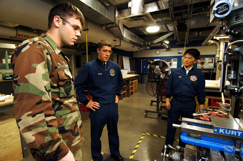 Senior cadet Christopher Allen explains procedures April 12 as he mills out one of the payloads for the upcoming vibration test of Falcon Satellite-5 to cadet seniors Colton Tuttle and Jae-Hyun Park. The satellite is being designed and built at the U.S. Air Force Academy in Colorado Springs, Colo. It will be tested and operated by the cadets through the USAFA Space Systems Research Center. (U.S. Air Force photo/Mike Kaplan)