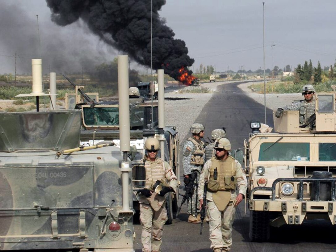 Waiting for explosive ordnance disposal to confirm the scene is safe, Staff Sgt. Christopher Hawks (left) and Master Sgt. Albert Schneider (right) prepare to collect evidence and obtain pictures in Iraq.  Sergeant Schneider's weapons intelligence team had just arrived at the scene of two improvised explosive devices detonations targeting. (U.S. Air Force photo)