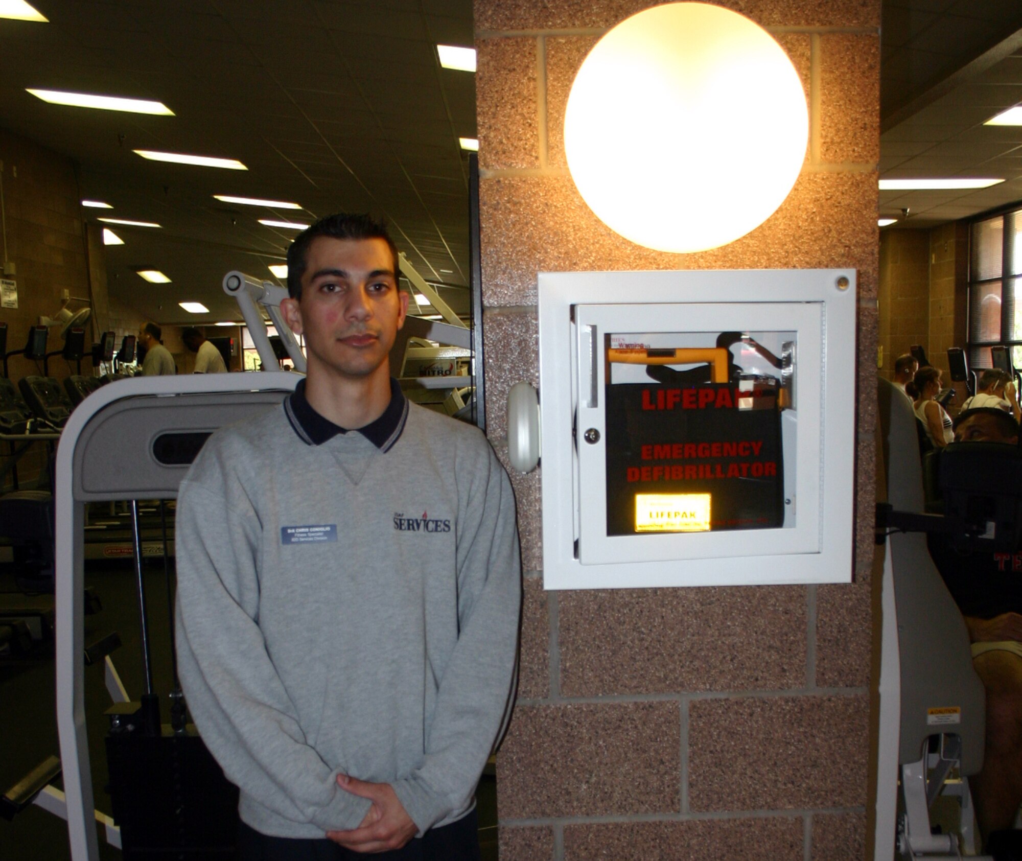 Senior Airman Christopher Coniglio stands alongside the AED he used to save the life of an OSI agent at the Levitow Fitness Center April 18. (U.S. Air Force photo/Staff Sgt. Tonnette Thompson)