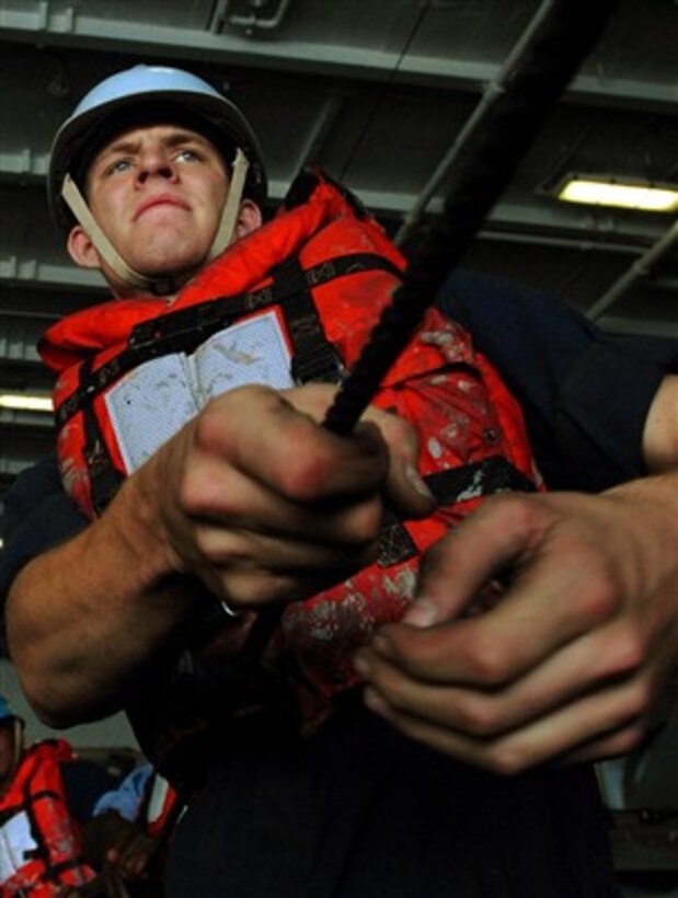 U.S. Navy Seaman Andrew Vanhuis hauls in a tending line in the hangar bay of the aircraft carrier USS John C. Stennis (CVN 74) during a replenishment at sea with the USNS Arctic (T-AOE 8) on April 5, 2007.  The John C. Stennis Carrier Strike Group is supporting maritime security operations in the Arabian Sea.  
