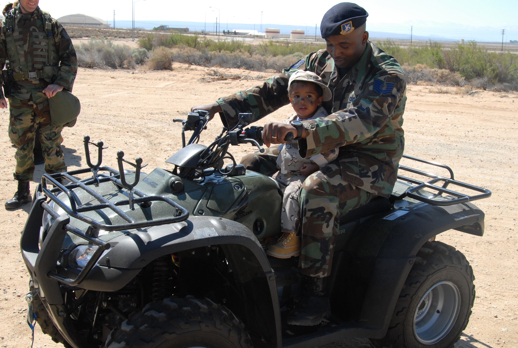 Tech. Sgt. Robert Tucker, 95th Security Forces Squadron police services noncommissioned officer in charge, assists his 1-year-old son, Christian, on an all-terrain vehicle during Operation KUDOS at the Oasis Community Center on Saturday. Operation KUDOS, or Kids Understanding Deployment Operations, is geared to provide Edwards children the opportunity to process through deployment lines and "deploy." (Photo by Airman Mikeal A. Young)