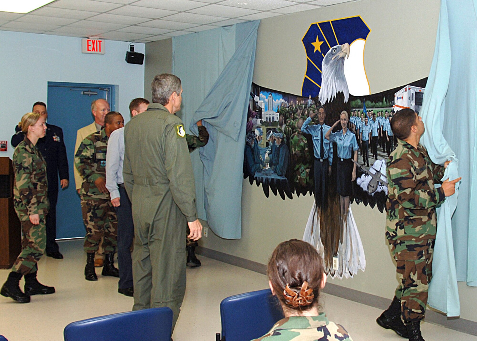 Security forces students, Airman Basics Adrien Quiles and Joseph Gussman unveil the finished Air Force Medical Service mural during a ceremony held April 24 at Camp Rissington on Lackland Air Force Base, Texas. The mural, created by artist Jacob Galey spans a 20-foot section of wall in the 59th Medical Wing Readiness Division's training classroom. It depicts the past, present and future of the medical corps. (U.S. Air Force photo/Staff Sgt. Ruth Stanley)