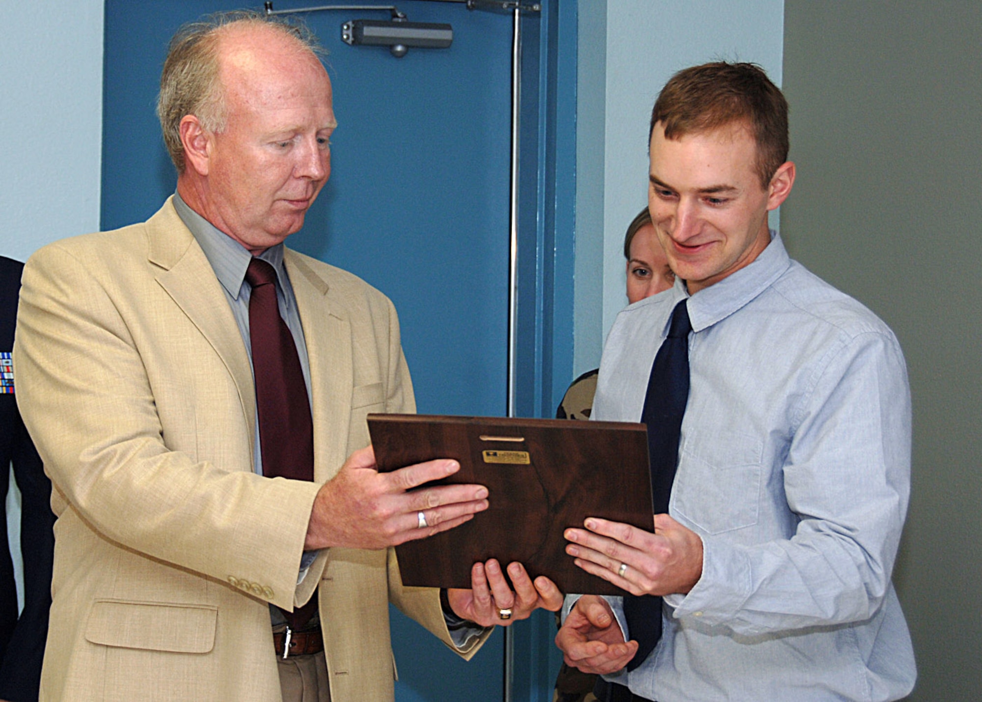 Artist Jacob Galey, husband of Capt. Lisa Mull a psychology resident with the 59th Medical Operations Squadron, receives a plaque from retired Maj. Ron Little at Camp Rissington, on Lackland Air Force Base, Texas, April 24. The plaque thanked Mr. Galey for his work on the Air Force Medical Service mural he painted on the Medical Unit Readiness Training site classroom wall for the 59th MDW Readiness Division. The mural depicts the past, present and future of the medical corps. (U.S. Air Force photo/Staff Sgt. Ruth Stanley)