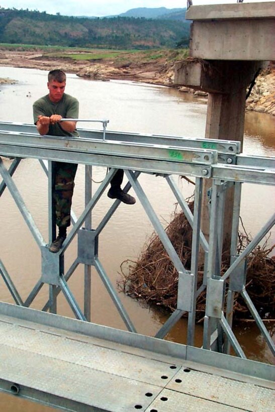 Marine Lance Cpl. Joseph Oliver works on the bridge at Ojo de Agua in Honduras. The new span, completed during the Christmas holiday season, replaced a concrete bridge in the background. Hurricane Mitch caused floods that swept away several 100-ton support columns of the old bridge, collapsing it. Cpl. Chet Decker, USMC