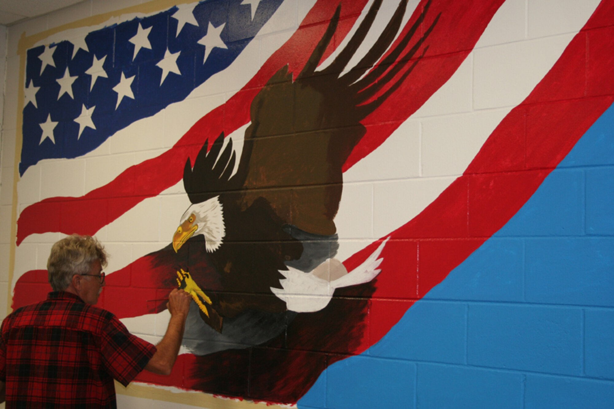 Jim Rahn puts touches on a bald eagle that is part of a mural on the wall of the deployment control center. Natalie Diel, wife of Tech. Sgt. Justin Diel, 20th Special Operations Squadron, spearheaded the project to brighten up the area where Airmen process for deployments. (U.S. Air Force photo by Airman Matthew Loken)