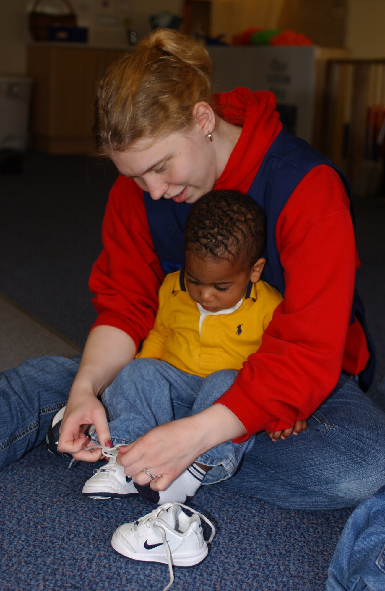 Karen Dodge, child development program assistant, ties the shoes of Aiko Smith before they go out to the playground at Child Development Center East on RAF Lakenheath April 26. (U.S. photo by Staff Sgt. Nicholasa Reed)