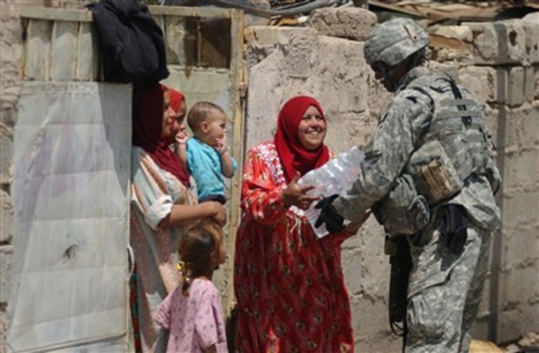 U.S. Army Master Sgt. John Paxton hands a container of drinking water to an Iraqi woman in the Al Murtada district of Mahmudiyah, Iraq, on April 19, 2007.  Paxton is attached to Alpha Company, 478th Civil Affairs Battalion.  