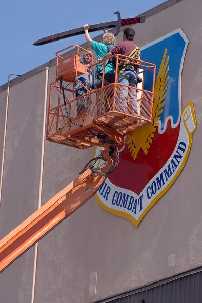 OFFUTT AIR FORCE BASE, Neb. -- Kay Barbara (center), a sign painter from the 55th Civil Engineer Squadron, assists John Abbod (right) and Ron Mona (left), 55th CES maintenance workers, in installing the sword on a new, freshly painted Air Combat Command Shield on Bldg. 305 April 18. (U.S. Air Force Photo by Josh Plueger)