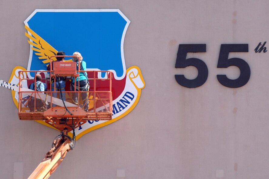 OFFUTT AIR FORCE BASE, Neb. -- Kay Barbara (right), a sign painter from the 55th Civil Engineer Squadron, assists John Abbod (middle) and Ron Mona (left), 55th CES maintenance workers, in installing the wings on a new, freshly painted Air Combat Command Shield on Bldg. 305 April 18. (U.S. Air Force Photo by Josh Plueger)