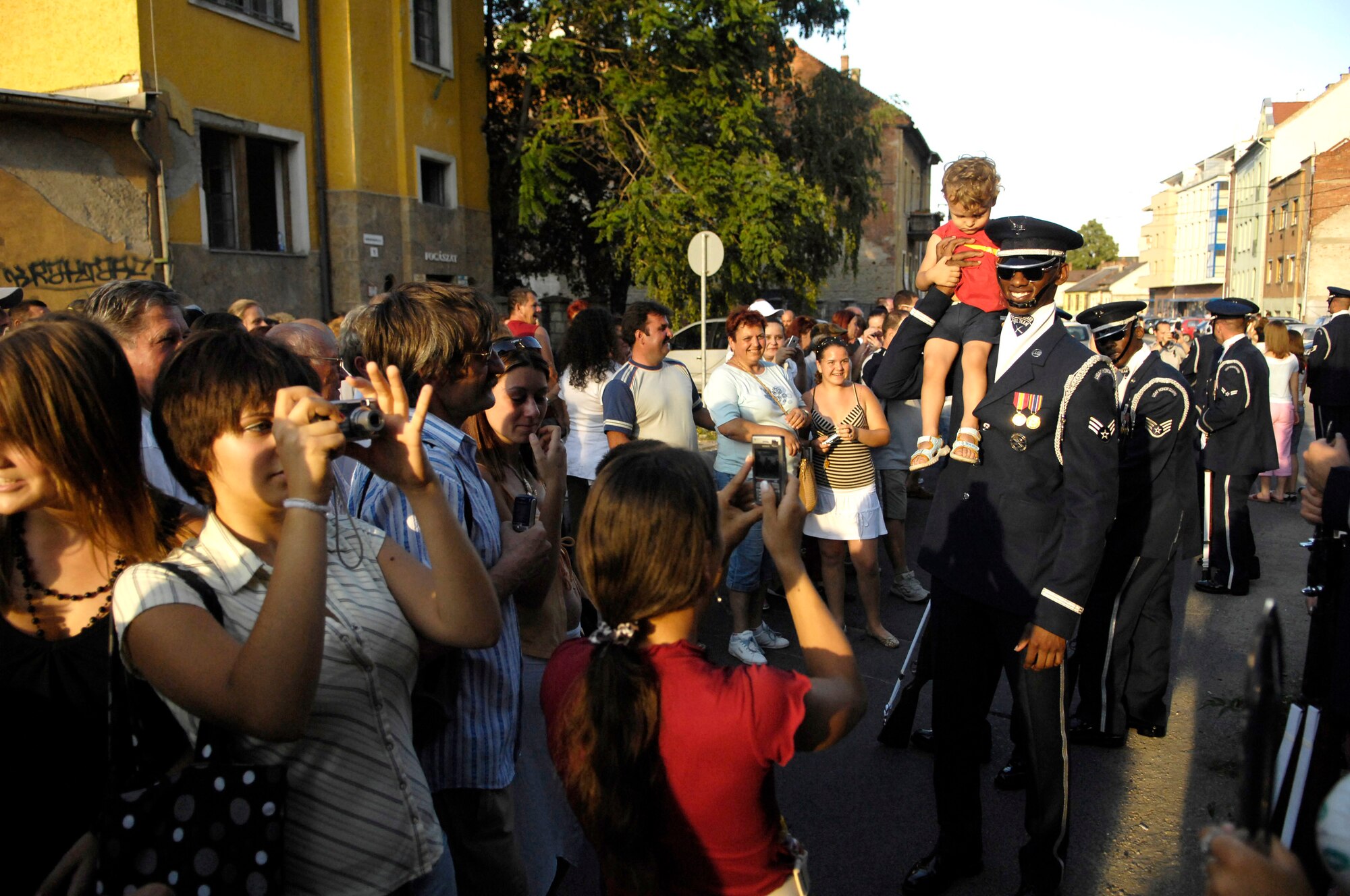 Senior Airman Jermaine James, a member of the U.S. Air Force Honor Guard Drill Team, lets a Hungarian child sit on his shoulder as parents take a picture in Miskolc City, Hungary, July 28. The drill team, the traveling component of the Air Force Honor Guard, is visiting three countries across central Europe. (U.S. Air Force photo/Senior Airman Daniel R. DeCook)