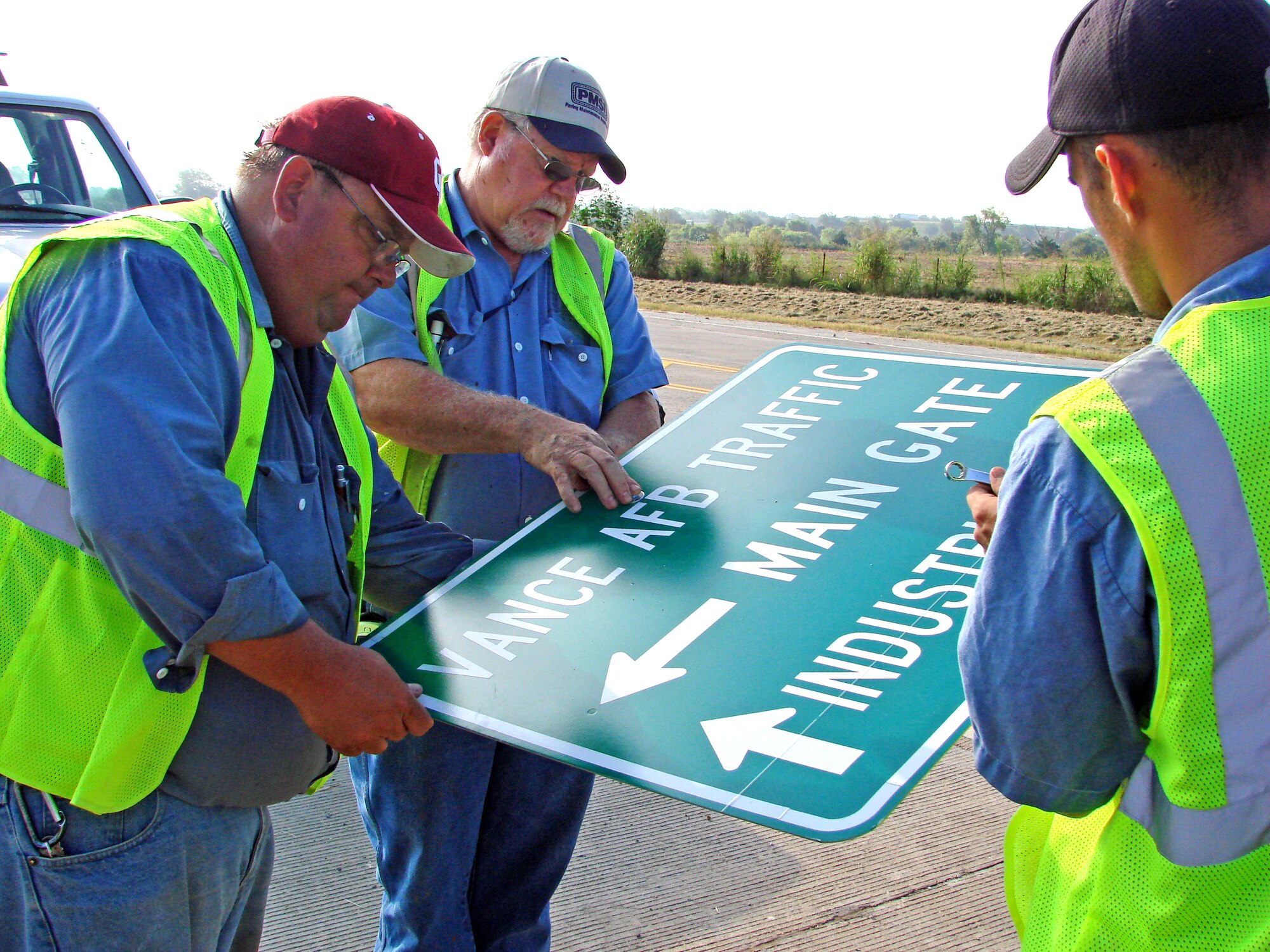 Mike Aguilar, Mike Goodpasture and Bill Hawkins, City of Enid Division of Traffic Control, prepare to post a sign on Southgate Road directing traffic to Vance Air Force Base. The traffic flow pattern to the base changes Aug. 16 when drivers coming to Vance from Van Buren Street will come to the Main Gate via Southgate and Gott Roads. Drivers coming from Cleveland St. will be able to access the base via the Industrial/West Gate during duty hours.  After duty hours, Industrial/West Gate and the perimeter fence access gate on Cleveland will be closed, requiring all vehicle traffic to access the base via Southgate. Drivers should be prepared for traffic delays during this transition period and should plan accordingly.            
