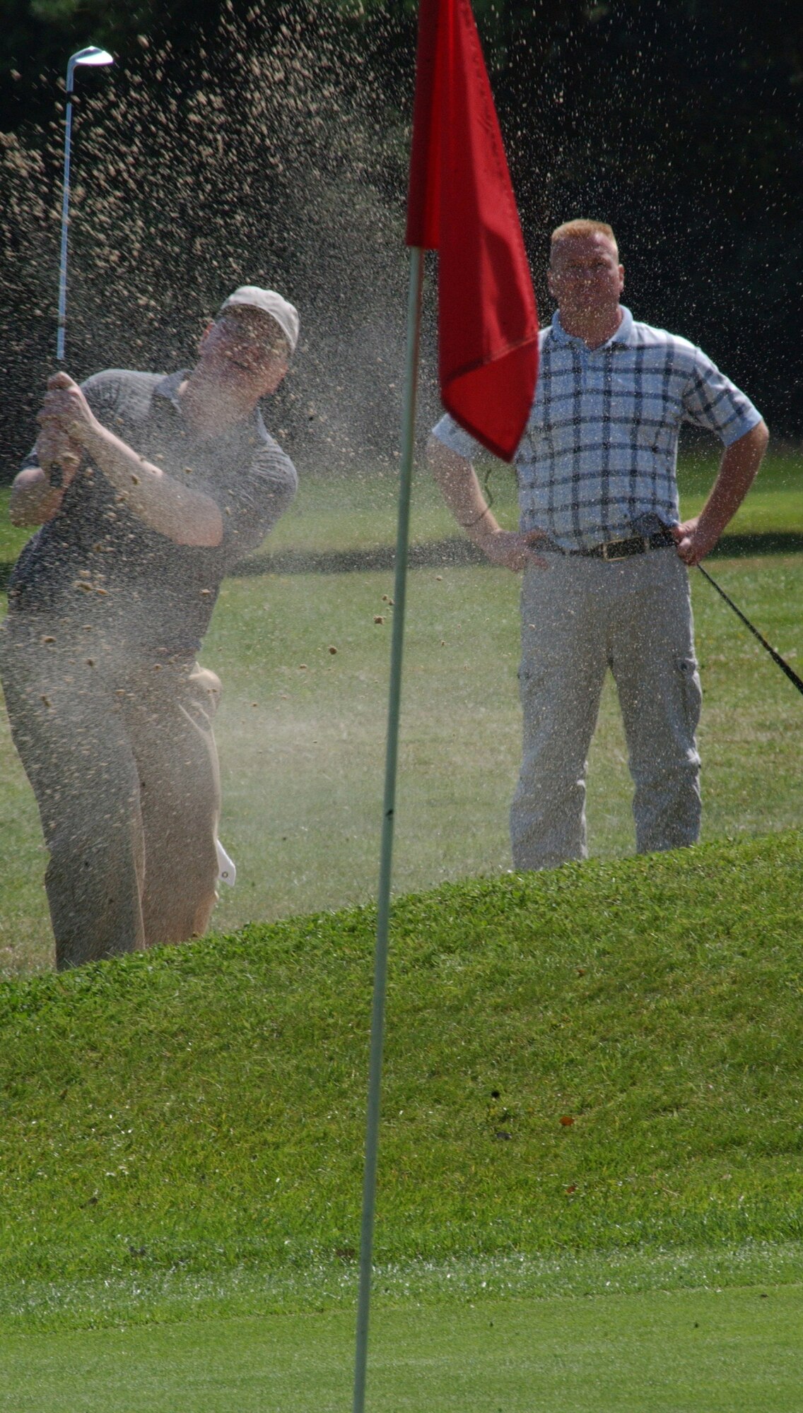 Tom Chatburn, playing for 373rd Training Squadron, blasts the ball out of the bunker at the 17th hole in the intramural golf league at the Breckland Pines Golf Club July 31. Teammate Jim Rose looks on. (Air Force photo by Airman Brad Smith)