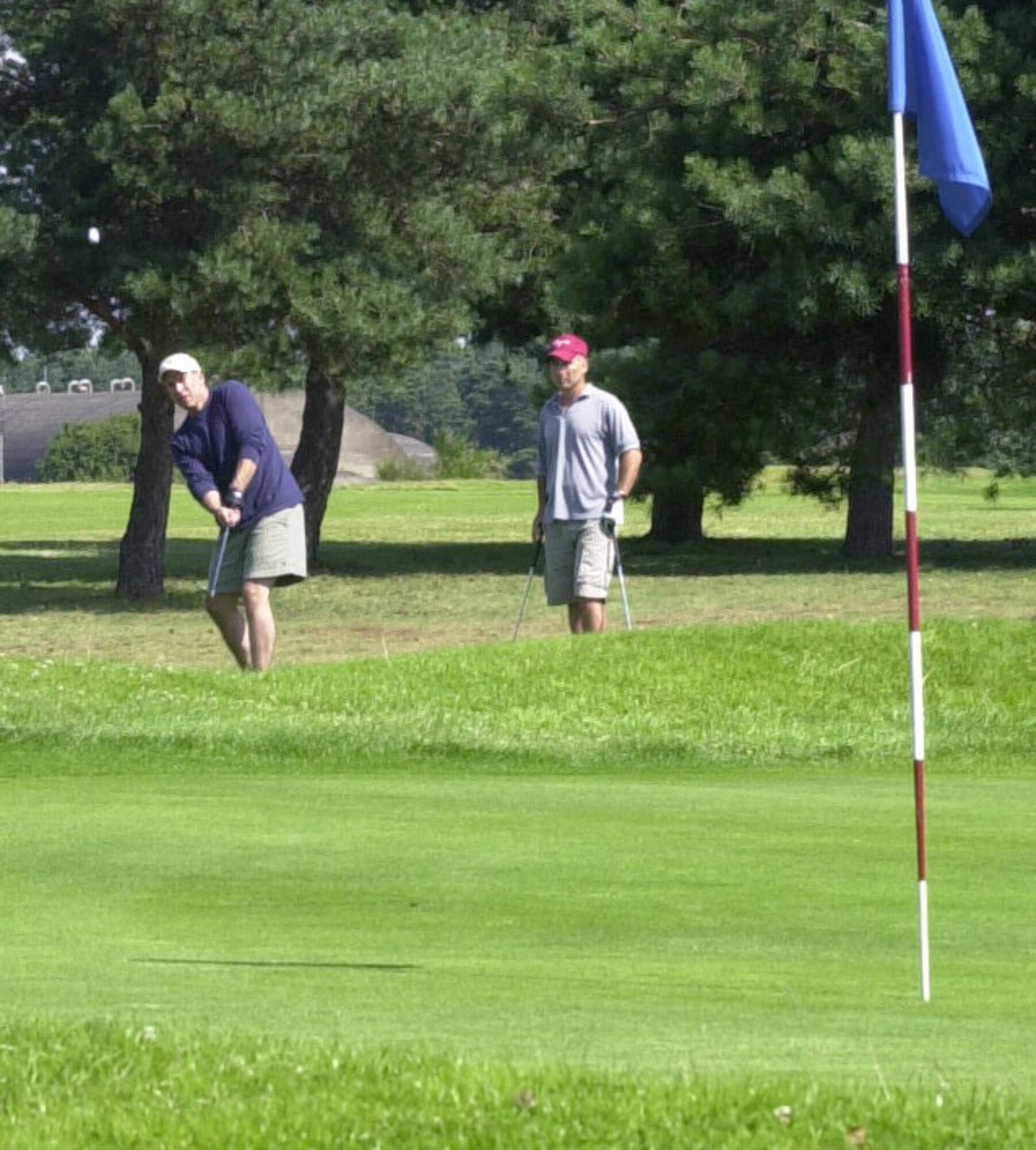 Joe Peery, playing for 100th Mission Support Squadron chips the ball on the 15th green in the intramural golf league at the Breckland Pines Golf Club July 31 with Mark Gagnon looking on. (Air Force photo by Gary Rogers)