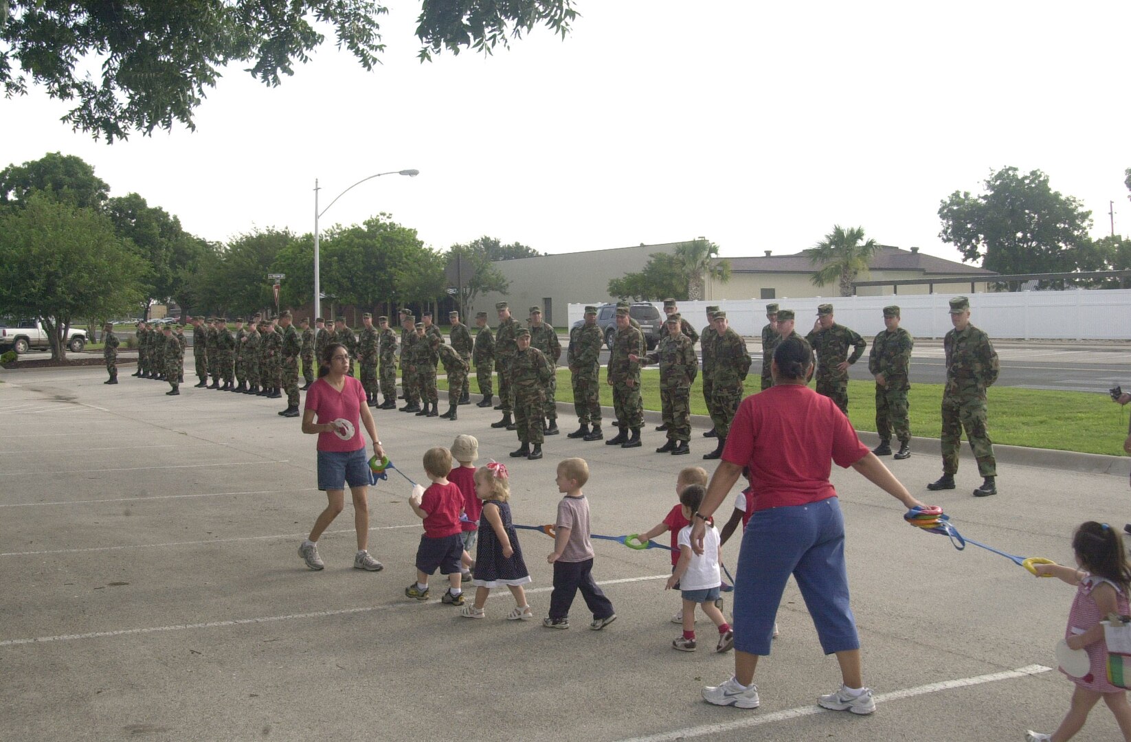 Students and staff members from the Goodfellow NCO Academy stand in formation as children, staff and parents from the Child Development Center walk in procession in front of the academy. The procession was part of the CDC’s small parade in celebration of Independence Day. (U.S. Air Force photo by Airman 1st Class Stephen Musal)