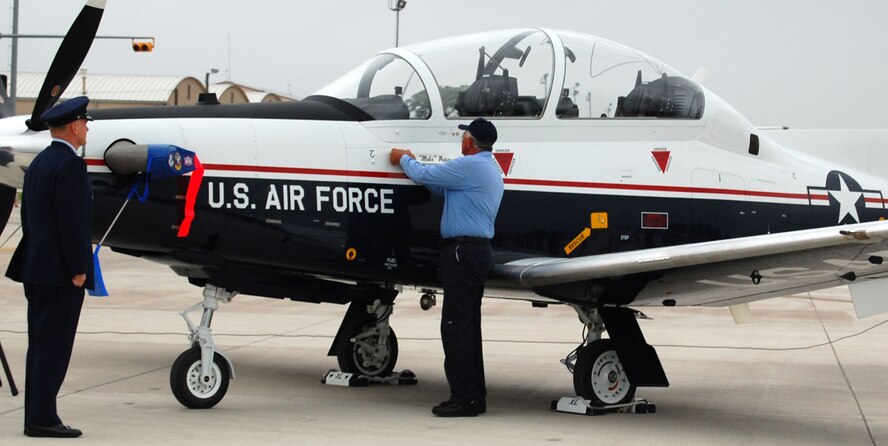 LAUGHLIN AIR FORCE BASE, Texas -- Col. Martin Schans, incoming 47th Operations Group Commander, watches as Robert Fellows, T-6 Texan II Aircraft Attendant, peels back the tape to reveal the new commanders name on a T-6 Texan II. Colonel Schans is taking over command for Col. David Peterson, outgoing 47th OG Commander.
 
 

