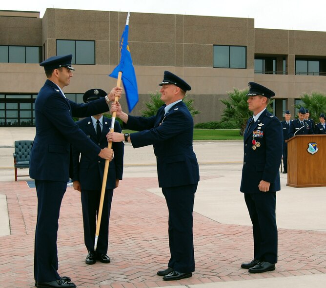 LAUGHLIN AIR FORCE BASE, Texas -- Col. Martin Schans, incoming 47th Operations Group Commander, receives the 47th OG's guidon from Col. Mike Minahan, 47th Flying Training Wing Commander, symbolizing the passing of command from one person to the next, while Col. David Peterson, outgoing 47th OG Commander, stands by Aug. 2.

