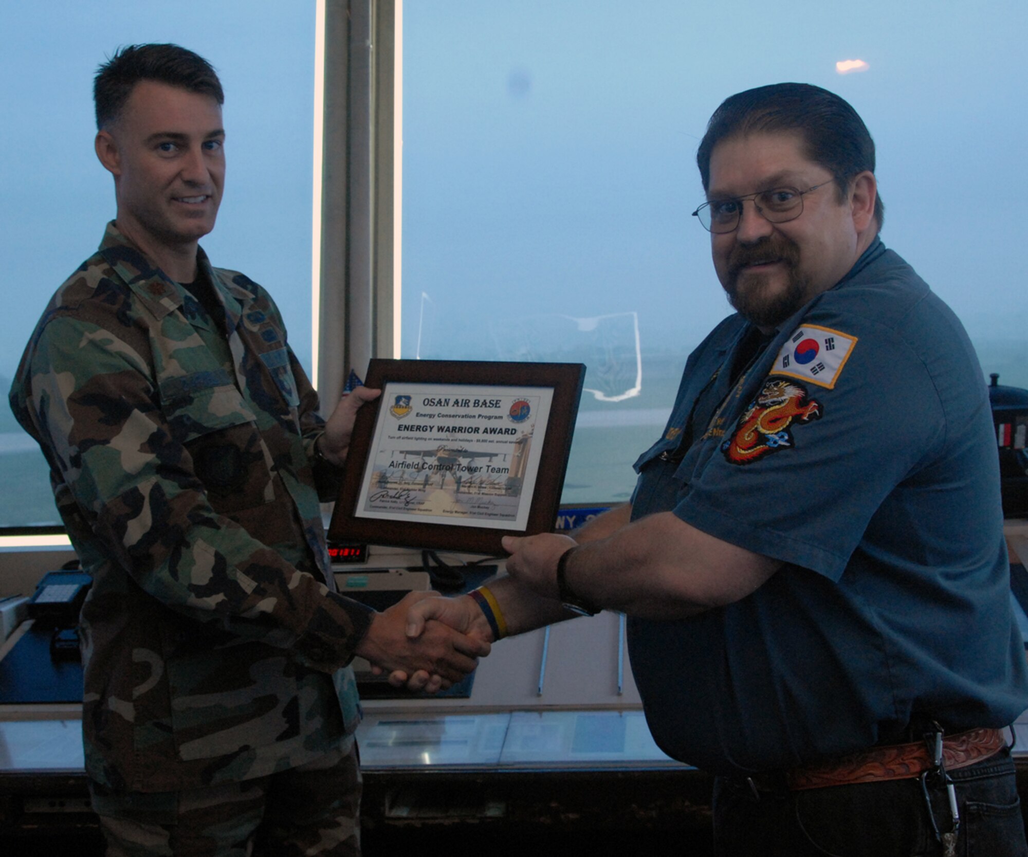 OSAN AIR BASE, Republic of Korea -- Mr. Jon Muckey, 51st Civil Engineer Squadron energy conservation team program manager, presents Maj. Bart Darnell, 51st Operations Support Squadron, with the Energy Warrior Certificate on Aug. 1 here. The 51st Fighter Wing Airfield Control Tower team recently received the first Osan
Energy Warrior Award for their efforts in energy conservation. 