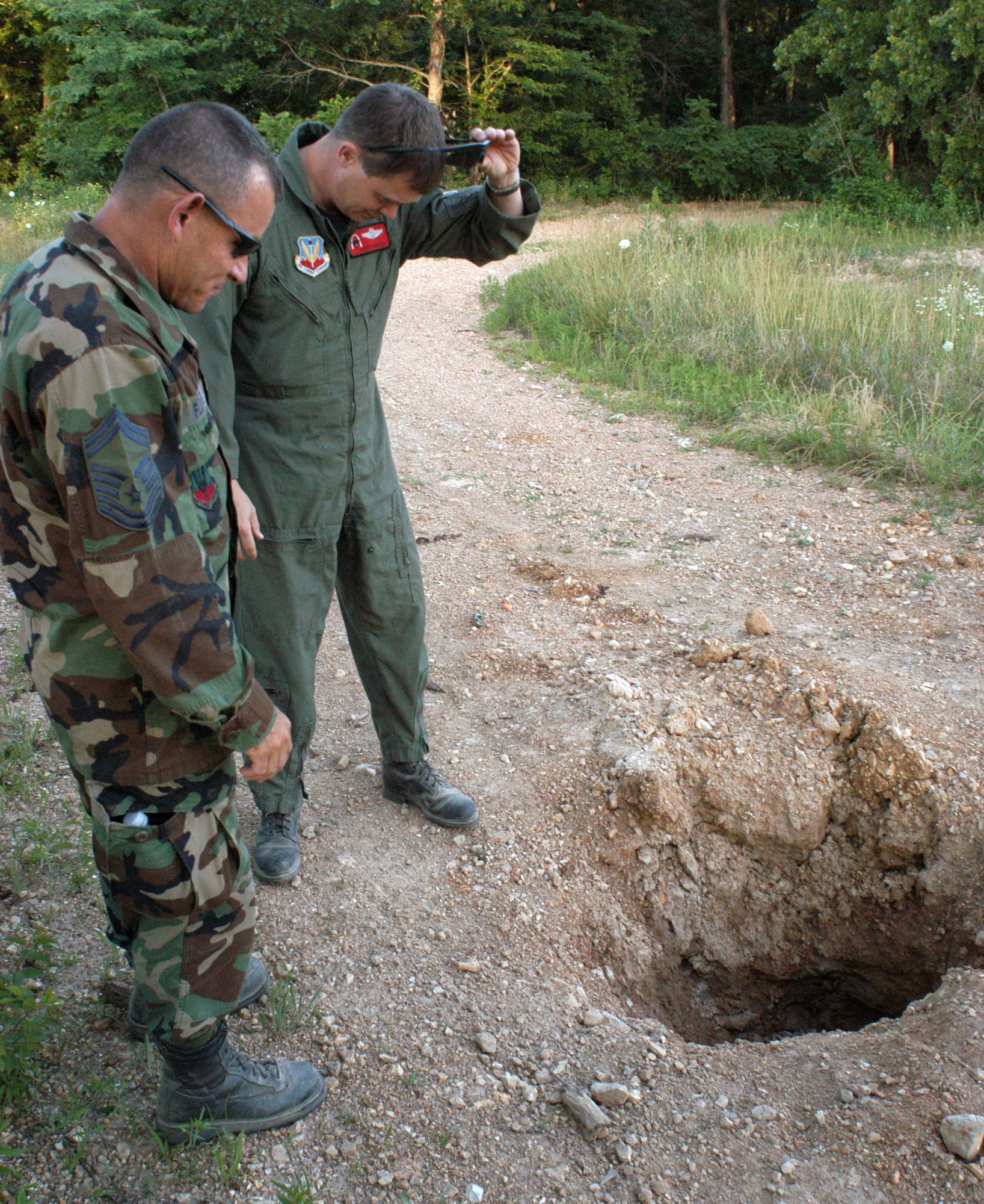 Senior Master Sgt. Randy Flores, left, and Lt. Col. Scott Porter examine a hole in a gravel road created by an inert 500-pound, concrete-filled practice bomb at Cannon Range near Ft. Leonard Wood, Mo., June 19, 2007.  Sergeant Flores is the range's superintendent and Colonel Porter is the range commander.  Repairing roads at the range is common due to natural degredation and the ordnance that rains down from Air Force Reserve, Air National Guard and active-duty planes, which use the range for training.  Both Airmen are members of the Missouri Air National Guard's 131st Fighter Wing, Detachment 1.  (U.S. Air Force photo/Maj. David Kurle)