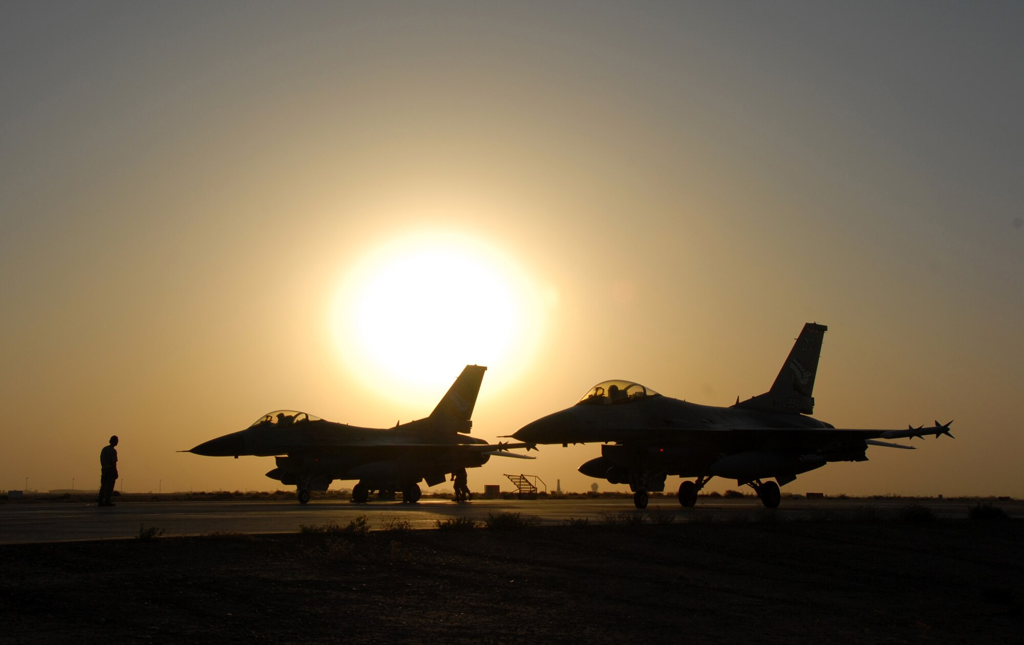A pair of F-16 Fighting Falcons sit on the flightline as the sun sets at Balad Air Base Iraq.  F-16s fly close-air-support missions exclusively for Operation Iraqi Freedom.  F-16s destroyed dirt bridges being used by insurgents Aug. 4 in Baghdad.  (U.S. Air Force photo/Tech. Sgt. Beth Holliker)