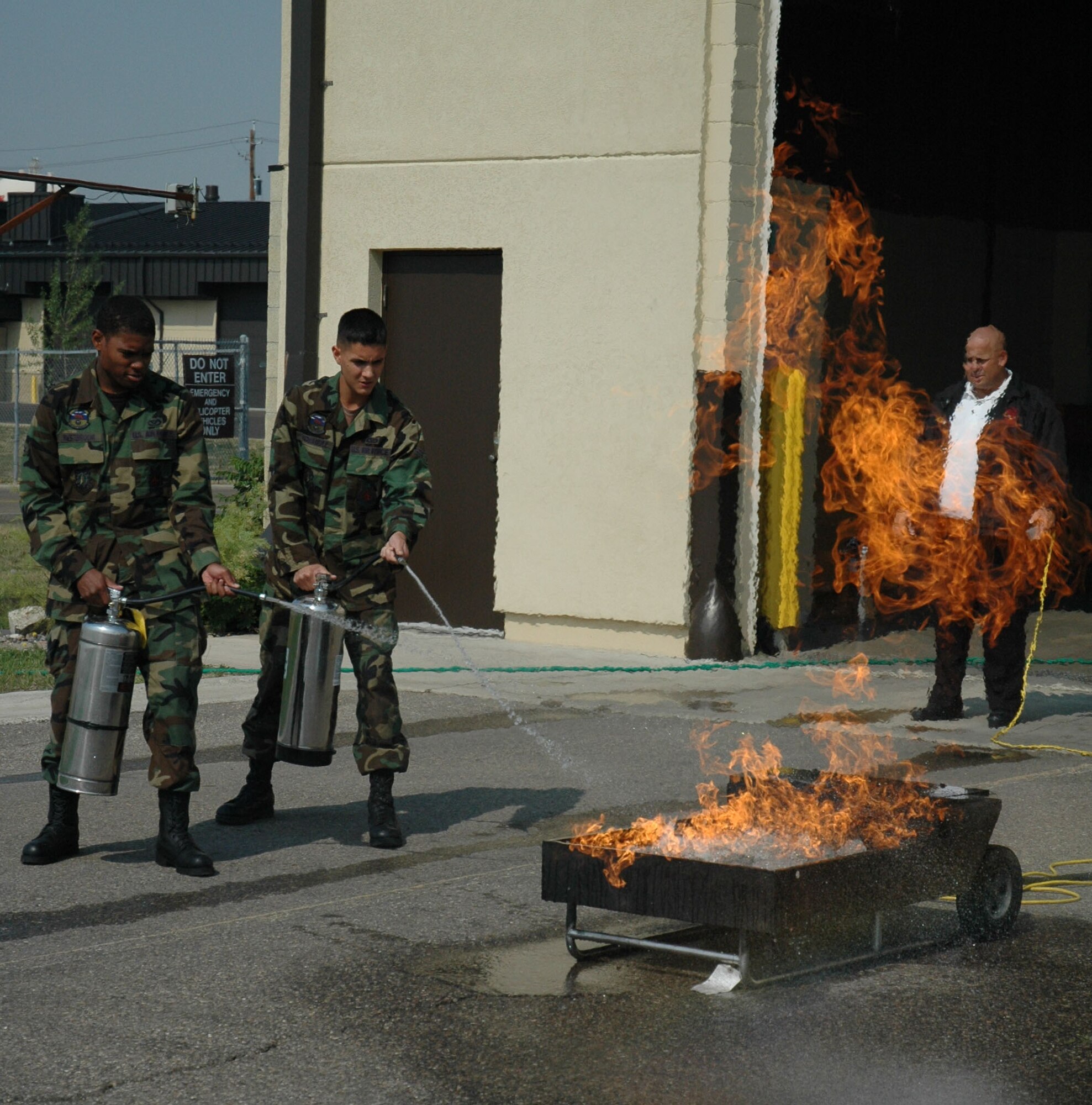 Airman Gerald Westbrook  and Airman 1st Class Juan Hernandez, 341st Civil Engineer Squadron fire fighters, demonstrate fire extinguishing procedures as Rickey Naccarato, 341st CES fire inspector, ignites the flames. (U.S. Air Force photo / Airman 1st Class Emerald Ralston)