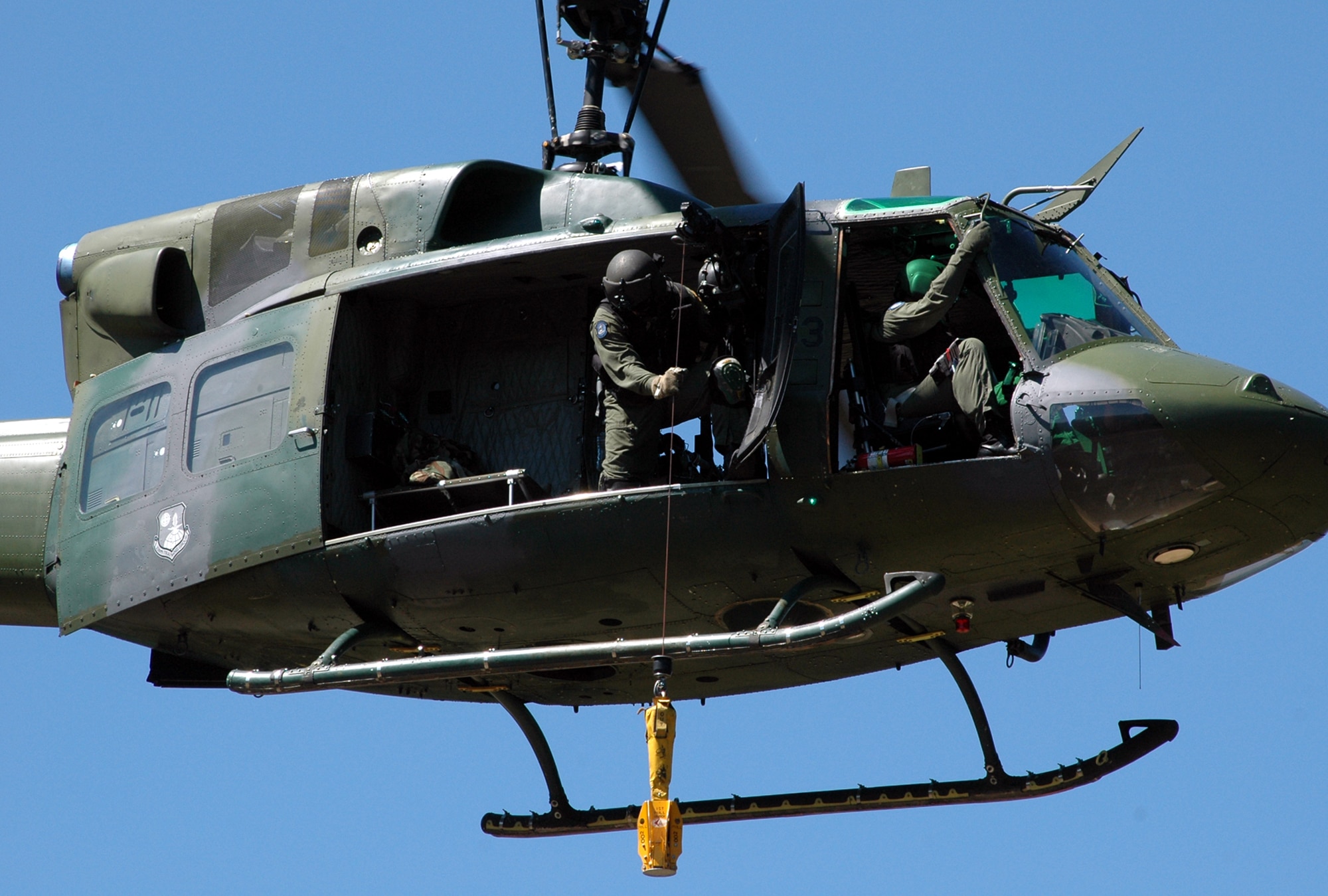 FAIRCHILD AIR FORCE BASE, Wash. -- During a training mission, Staff Sgt. Jamie Aulbach, 36th Rescue Flight UH-1N Huey flight engineer, lowers a forest-penetrating device down from the side of the helicopter during precision alternate insertion and extraction drills. The flight engineer picks a point on the ground and tries to hit it with the hoist. Flight engineers must retain currency by successfully maneuvering a certain number of hoists per quarter. (U.S. Air Force Photo / Tech. Sgt. Larry W. Carpenter Jr.) 