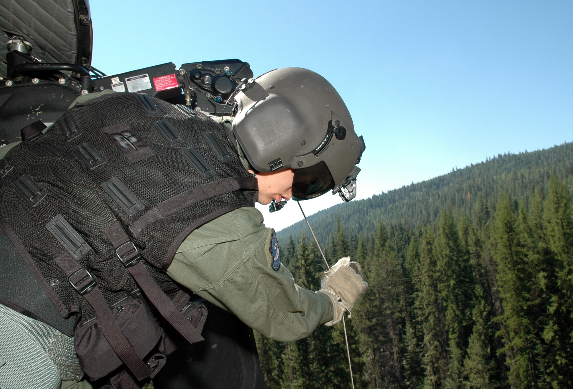 FAIRCHILD AIR FORCE BASE, Wash. -- During a training mission, Staff Sgt. Jamie Aulbach, 36th Rescue Flight UH-1N Huey flight engineer, lowers a forest-penetrating device from the side of the helicopter during precision alternate insertion and extraction drills. Sergeant Aulbach pushes out on the cable, ensuring the cable does not make contact with the skid, which could cause the cable could fray and break. (U.S. Air Force Photo / Tech. Sgt. Larry W. Carpenter Jr.) 