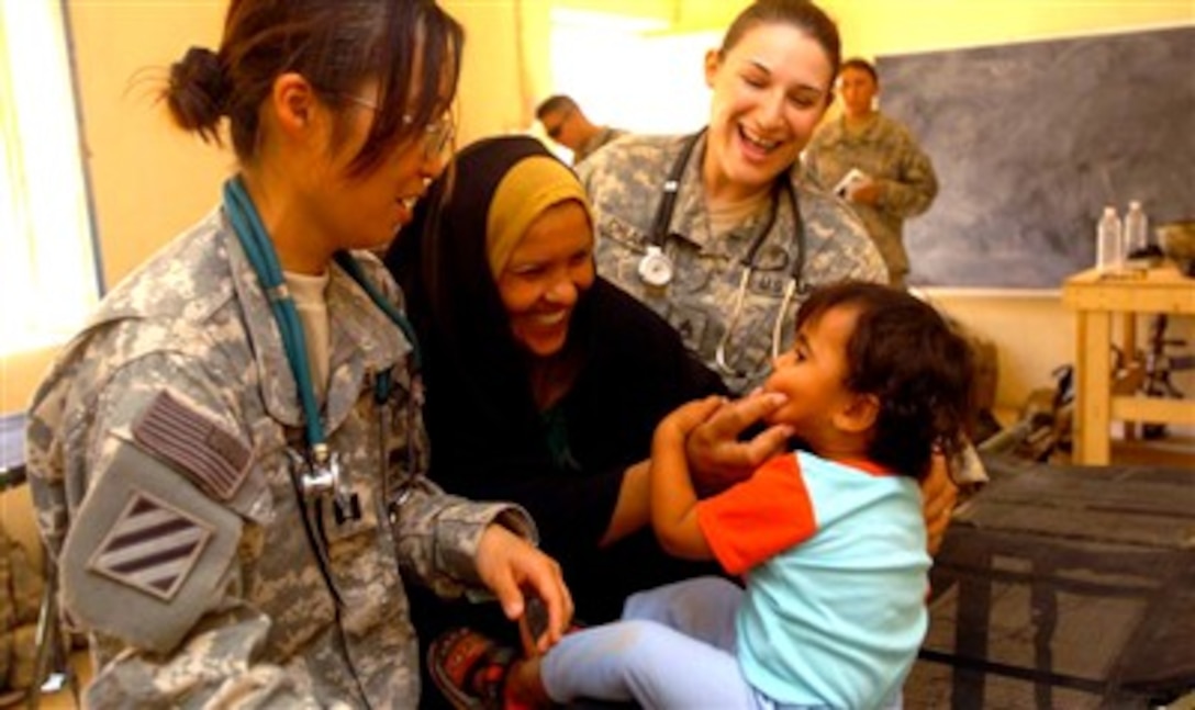 U.S. Army Capt. Se Young Um, a pediatrician and surgeon assigned to the 203rd Brigade Support Battalion, and Staff Sgt. Jade Chiara, a non-commissioned officer in charge of the aid station at Forward Operating Base Hammer, smile and listen as a mother explains the symptoms of her child's ailment, Aug. 5, 2007, during a free medical clinic at a school in Al Zatia, Iraq. 