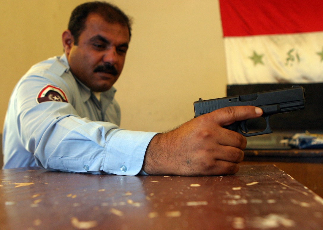 AL QA?IM DISTRICT HEADQUARTERS POLICE STATION, AL QA?IM, Iraq ? An Iraqi policeman, or IP, with the Al Qa?im district police proudly holds his pistol while the Iraqi flag hangs in the background.  The police here have grown up with the townspeople thus creating a close bond with one another.