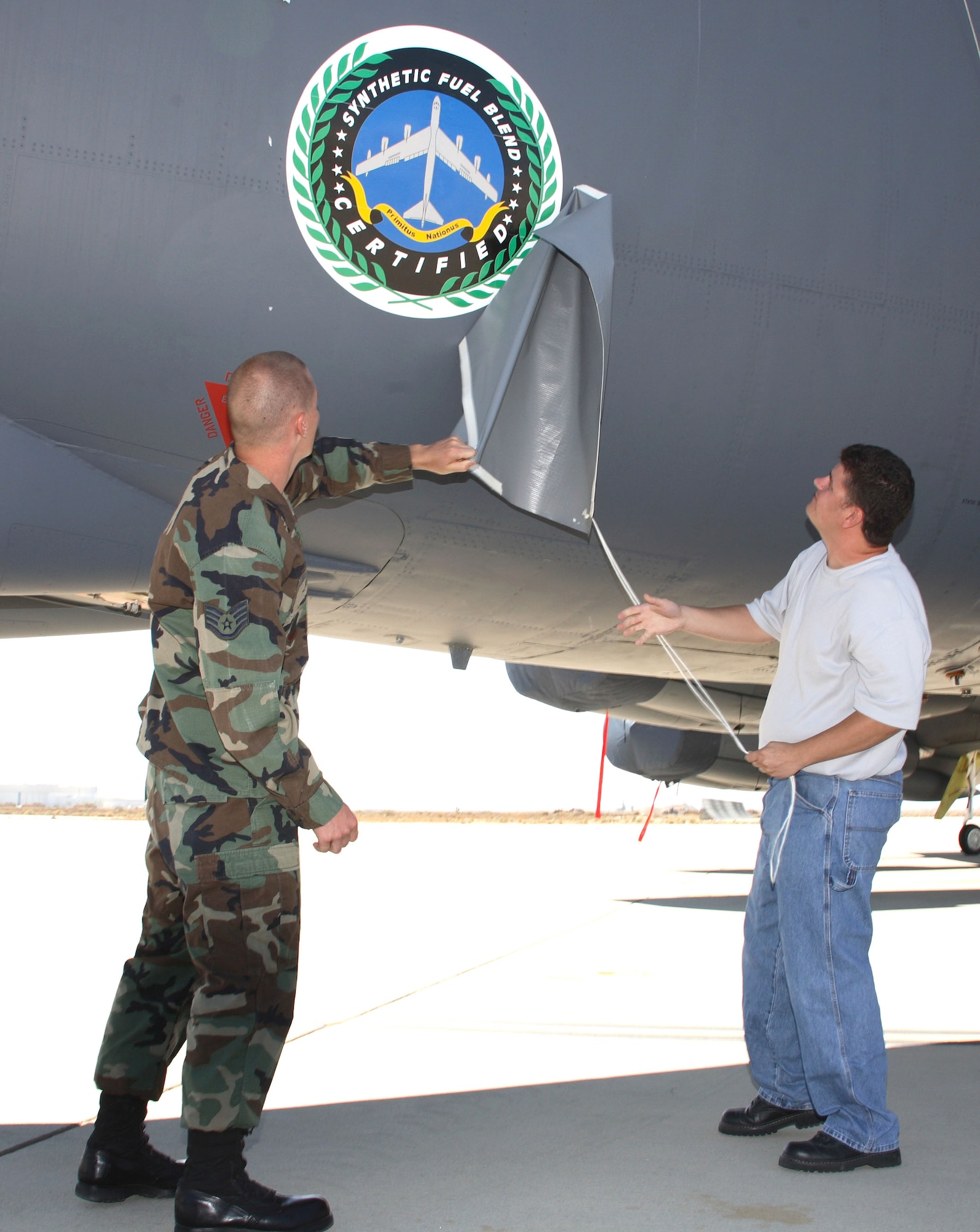 Staff Sgt. Joe Wallis and Johnny Sniderhan reveal the Fischer-Tropsch synthetic fuel blend certification logo painted on the side of a B-52H Stratofortress at the certification ceremony at Edwards Air Force Base, Calif., Aug. 8. Sergeant Wallis is with the 31st Test and Evaluation Squadron; Mr. Sniderhan is with the 912th Aircraft Maintenance Squadron. (U.S. Air Force photo/Jet Fabara)  