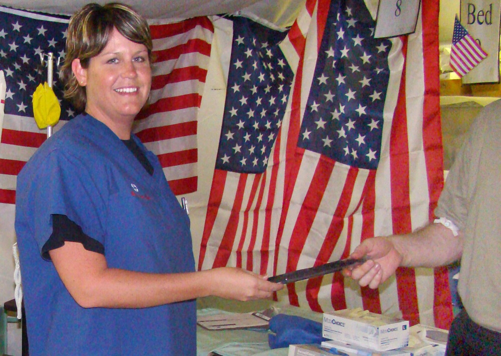 BALAD AIR BASE, Iraq -- Master Sgt. Sherry Hertlein, deployed to the 332 Expeditionary Medical Group from Cannon Air Force Base, N.M., hands an 'Ice Pop' to a patient at the Air Force Theater Hospital.  On 120-degree days in Iraq, air conditioners labor to maintain bearable temperatures in the tents of the field hospital. Patients found the icy treats to be a welcome relief heat, Sergeant Hertlein said. The ?Ice Pops? were donated by the communities from Cannon and Sergeant Hertlein's home town of Emporia, Kansas. The wounded Soldier in the photo is not identified in to protect his protect his privacy as a medical patient. ?Thanks to the many people who generously donated, we've reached a level that will sustain us through the summer,? she said. This month the hospital staff moves operations into a new, prefabricated building, which will have better insulation and air conditioning than the tents of the existing facility. (U.S. Air Force photo / Chief Master Sgt. Charles Cole)