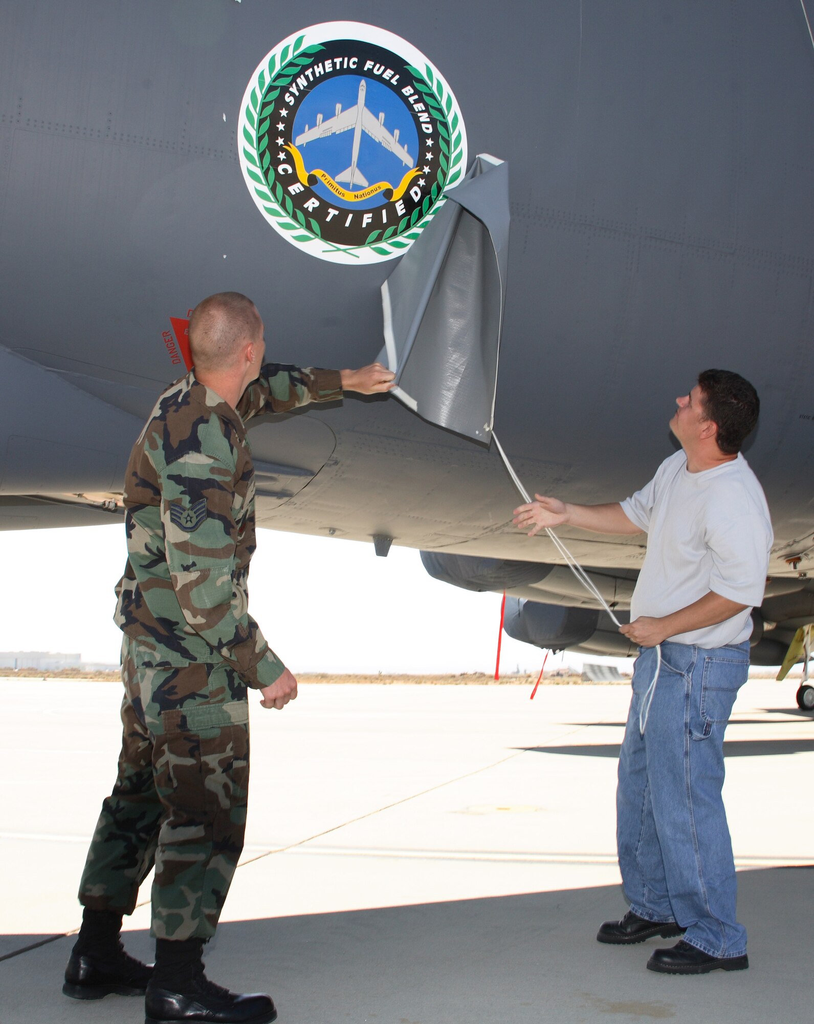 EDWARDS AIR FORCE BASE, Calif. -- Staff Sgt. Joe Wallis, 31st Test and Evaluation Squadron, and Johnny Sniderhan, 912th Aircraft Maintenance Squadron, reveal the Fischer-Tropsch synthetic fuel blend certification logo painted on the side of a B-52H at the certification ceremony here Aug. 8. (Photo by Jet Fabara)