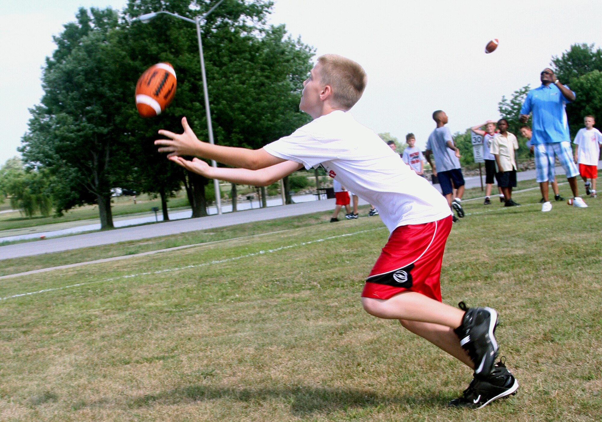 WHITEMAN AIR FORCE BASE, Mo. - Ryan Burk, son of Michelle and Tech. Sgt. Randy Burk, 509th Operations Support Squadron, receives a pass from Neil Smith Aug. 8 during a youth football clinic at the base soccer field. Neil Smith helped teach children the fundamentals of football during the clinic. He is currently a co-owner of the Kansas City Brigade and has played as a defensive lineman for the Kansas City Chiefs, the Denver Broncos and the San Diego Chargers. He has won two National Football League championship rings for Super Bowls XXXII and XXXIII. (U.S. Air Force photo/Airman 1st Class Stephen Linch)