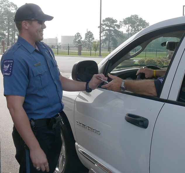 Buddy McNeal, USProtect gate guard, checks the identification of an incoming motorist Aug. 8. Mr. McNeal balanced family life with attending school and working full-time, and recently earned a commission to become an Air Force officer. He is slated to leave for pilot training at Columbus Air Force Base, Miss., in the fall. (U.S. Air Force photo by Airman 1st Class Eric Schloeffel)