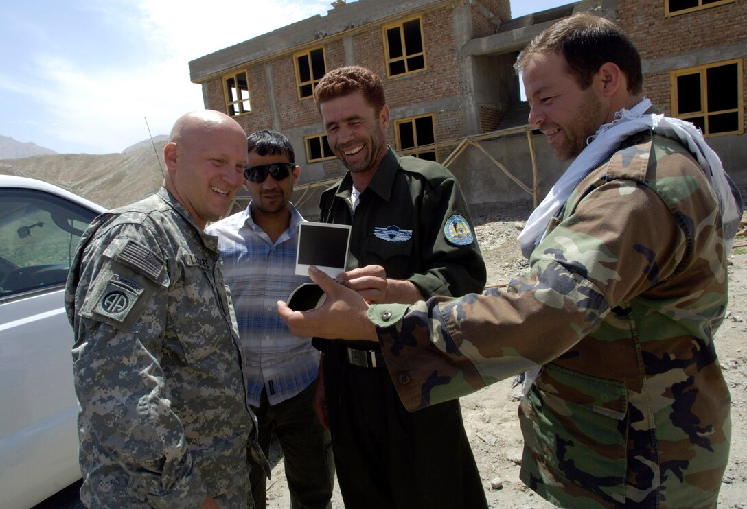 Panjshir Provincial Reconstruction Team commander Lt. Col. Christopher Luedtke (left) and Anaba district police chief Zardot Towhidi (center) share a laugh over some photos they took Aug. 6 during a training session. Colonel Luedtke brought members of his PRT to the Anaba district of Panjshir province, Afghanistan, to provide training to Afghan National Police serving in the area. Colonel Luedtke is deployed from Hill Air Force Base, Utah. (U.S. Air Force photo/Master Sgt. Jim Varhegyi)