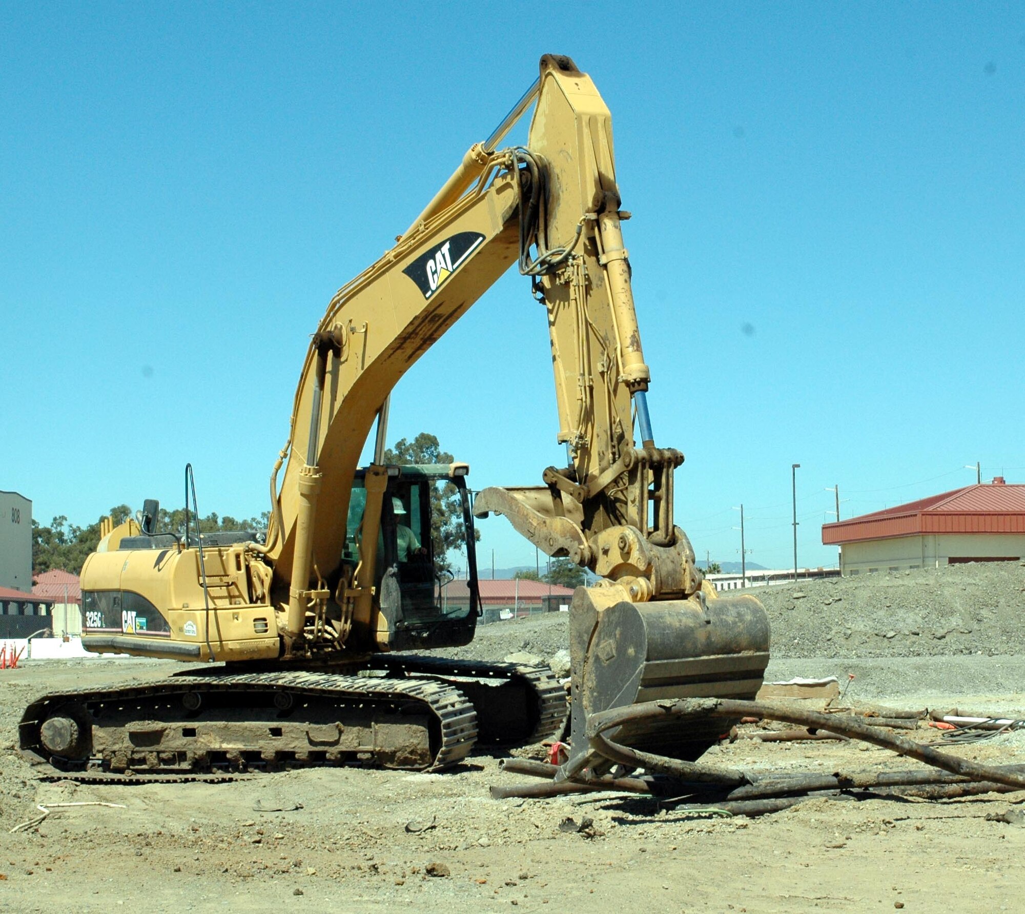 A worker operating a backhoe works to scoop up a piece of piping at the future site of the Aerospace Ground Equipment building. (U.S. Air Force photo/ Nick DeCicco)