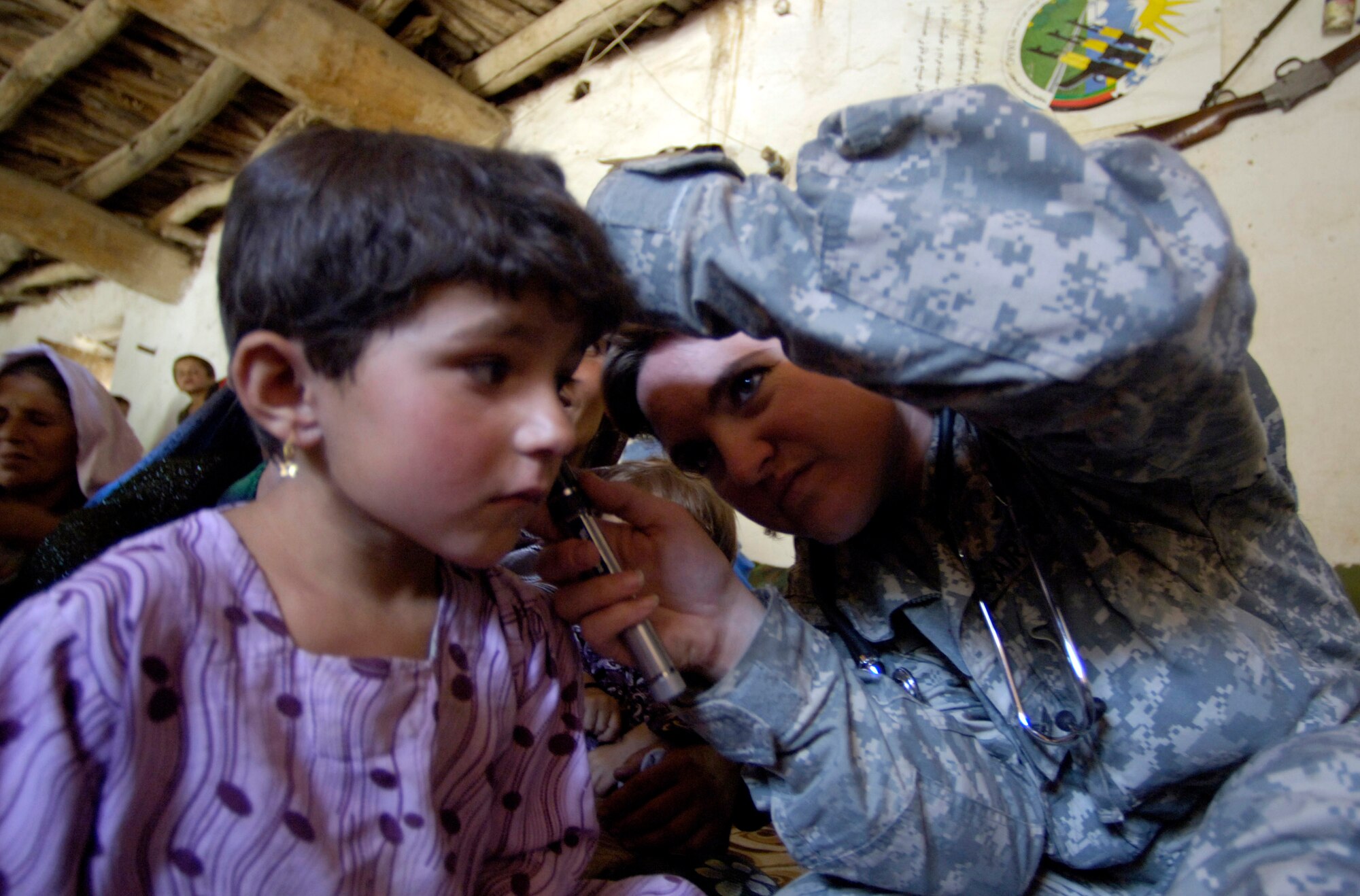 Panjshir Provincial Reconstruction Team member Tech. Sgt. Jenina Rose looks at a village girl's ears Aug. 7 in Roydara village in the Shutol district of Panjshir province, Afghanistan. Sergeant Rose is a medical technician deployed from Mountain Home Air Force Base, Idaho. She and her fellow PRT members made an 11-mile round-trip trek over a mountain pass and into a river valley to provide medical care to Afghans living in Roydara. (U.S. Air Force photo/Staff Sgt. Julie Weckerlein)
