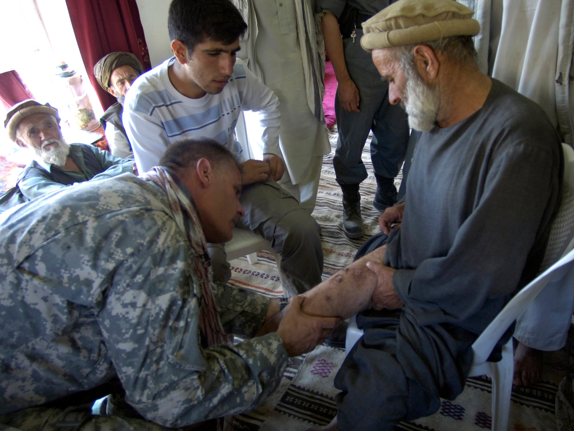 Panjshir Provincial Reconstruction Team member Capt. Kevin Kubly looks at sores on a villager's leg Aug. 7 in Roydara village in the Shutol district of Panjshir province, Afghanistan. Captain Kubly is a physician's assistant deployed from the 3rd Medical Group at Elmendorf Air Force Base, Alaska. He and his fellow PRT members made an 11-mile round-trip trek over a mountain pass and into a river valley to provide medical care to Afghans living in Roydara. (U.S. Air Force photo/Master Sgt. Jim Varhegyi)
