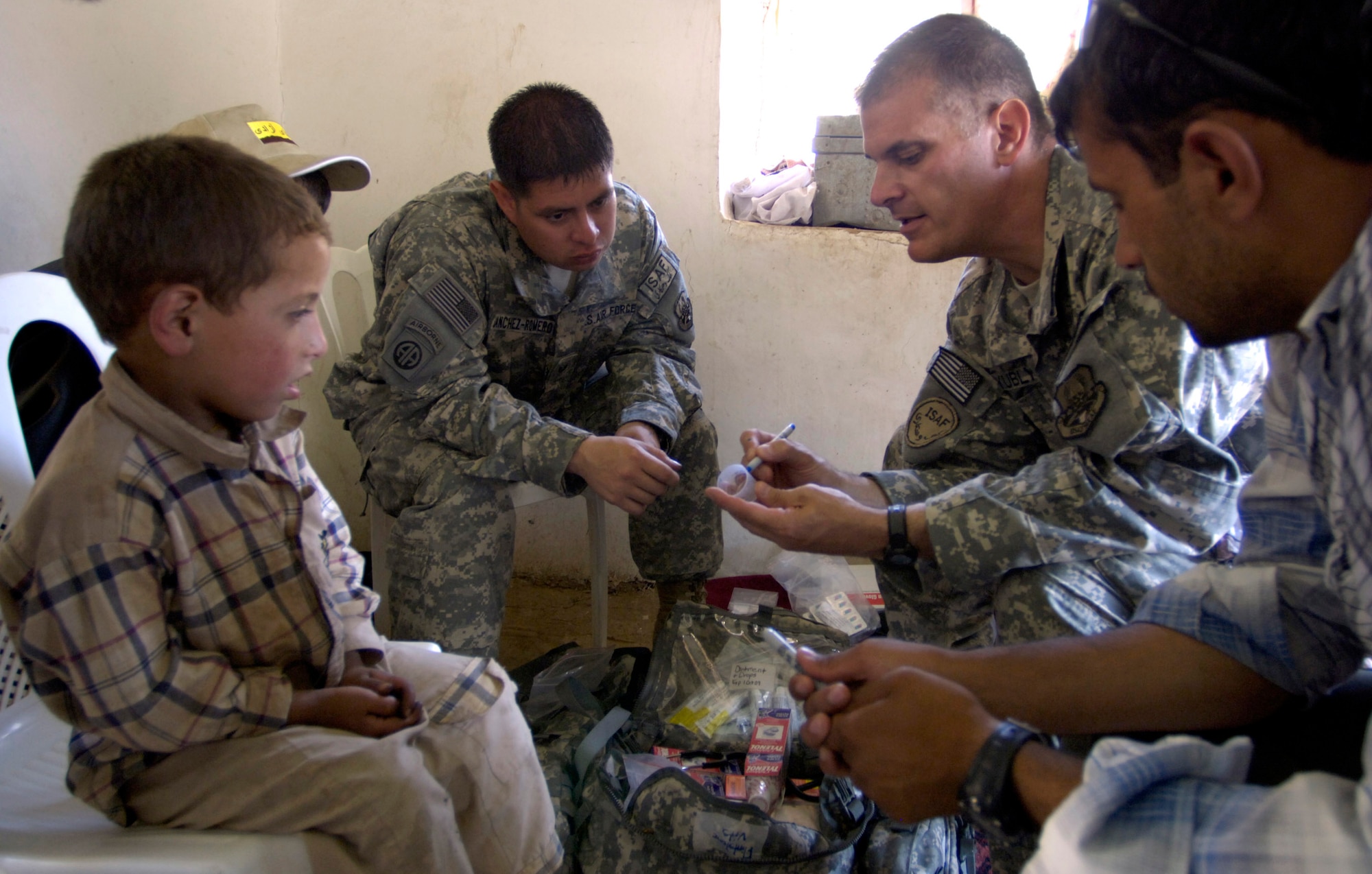 Panjshir Provincial Reconstruction Team members Capt. Kevin Kubly (second from right) and Staff Sgt. Andre Sanchez-Romero explain medication dosage through an interpreter to a village boy and his father (out of the picture) Aug. 7 in Roydara village in the Shutol district of Panjshir province, Afghanistan. Captain Kubly is a physician's assistant deployed from the 3rd Medical Group at Elmendorf Air Force Base, Alaska. Sergeant Sanchez-Romero is a security forces member deployed from Minot AFB, N.D. They and their fellow PRT members made an 11-mile round-trip trek over a mountain pass and into a river valley to provide medical care to Afghans living in Roydara. (U.S. Air Force photo/Master Sgt. Jim Varhegyi)
