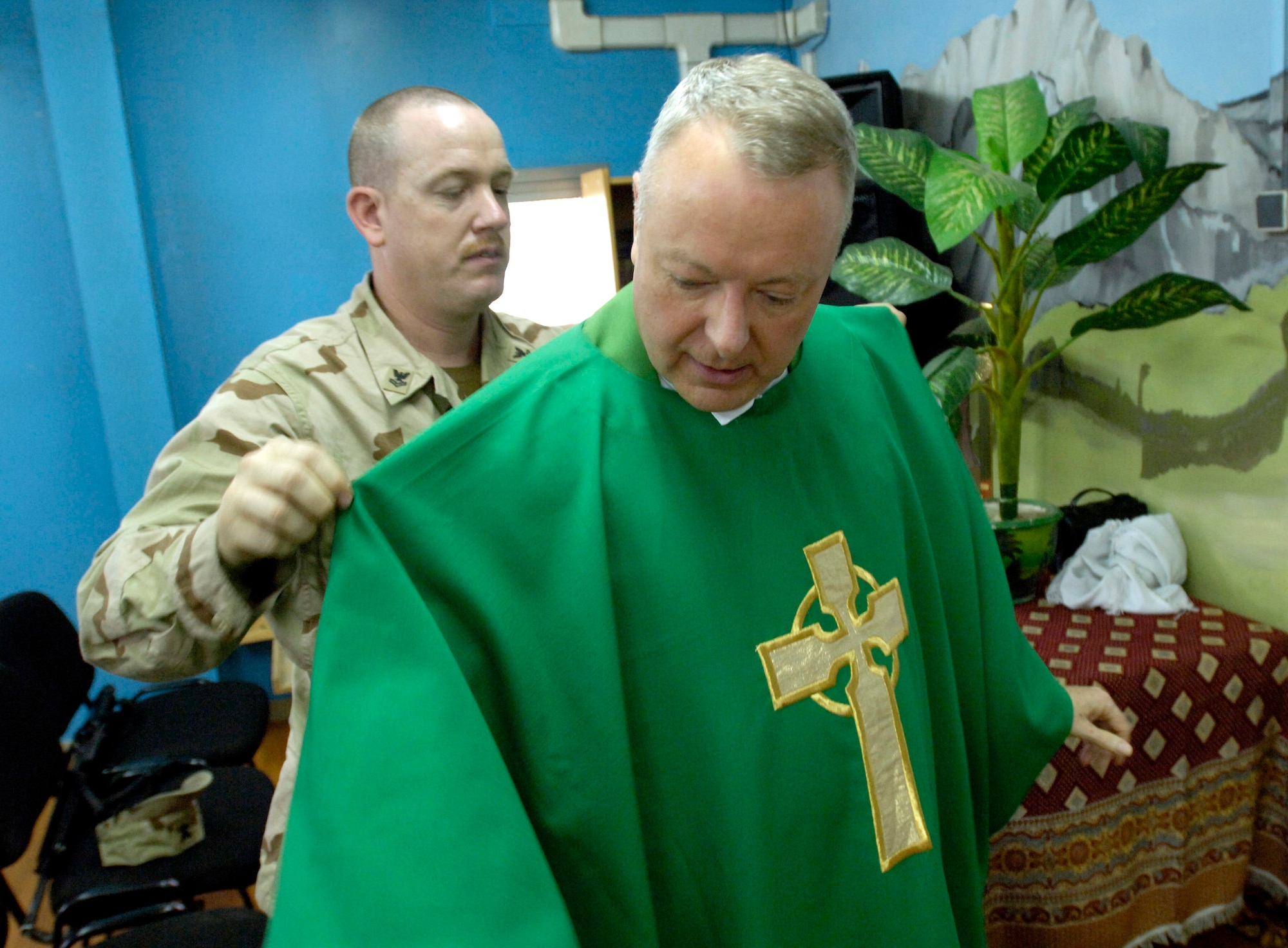 Navy Petty Officer 2nd Class Fred Hays assists Chaplain (Lt. Col.) Michael Weber into his vestments prior to the Catholic daily mass July 23 at Camp Eggers in Kabul, Afghanistan.  Besides providing the various chaplain services to the joint military community at Camp Eggers, Chaplain Weber also serves as a mentor to the Afghan Religious and Cultural Affairs officers, who are the Afghan equivalent to U.S. military chaplains.  Petty Officer Hays is a religious program specialist.  (U.S. Air Force photo/Master Sgt. Jim Varhegyi)