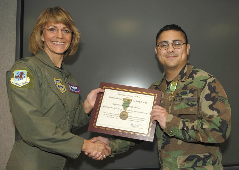 Col. Margaret Woodward, 89th Airlift Wing commander, presents an award citation after pining a Legion of Merit Medal to the collar of Senior Airman Joseph Vasquez. Airman Vasquez is assigned to the 89th Communications Squadron as a radio operator. The Legion of Merit is an award, which is given for service rendered in a clearly exceptional manner. 