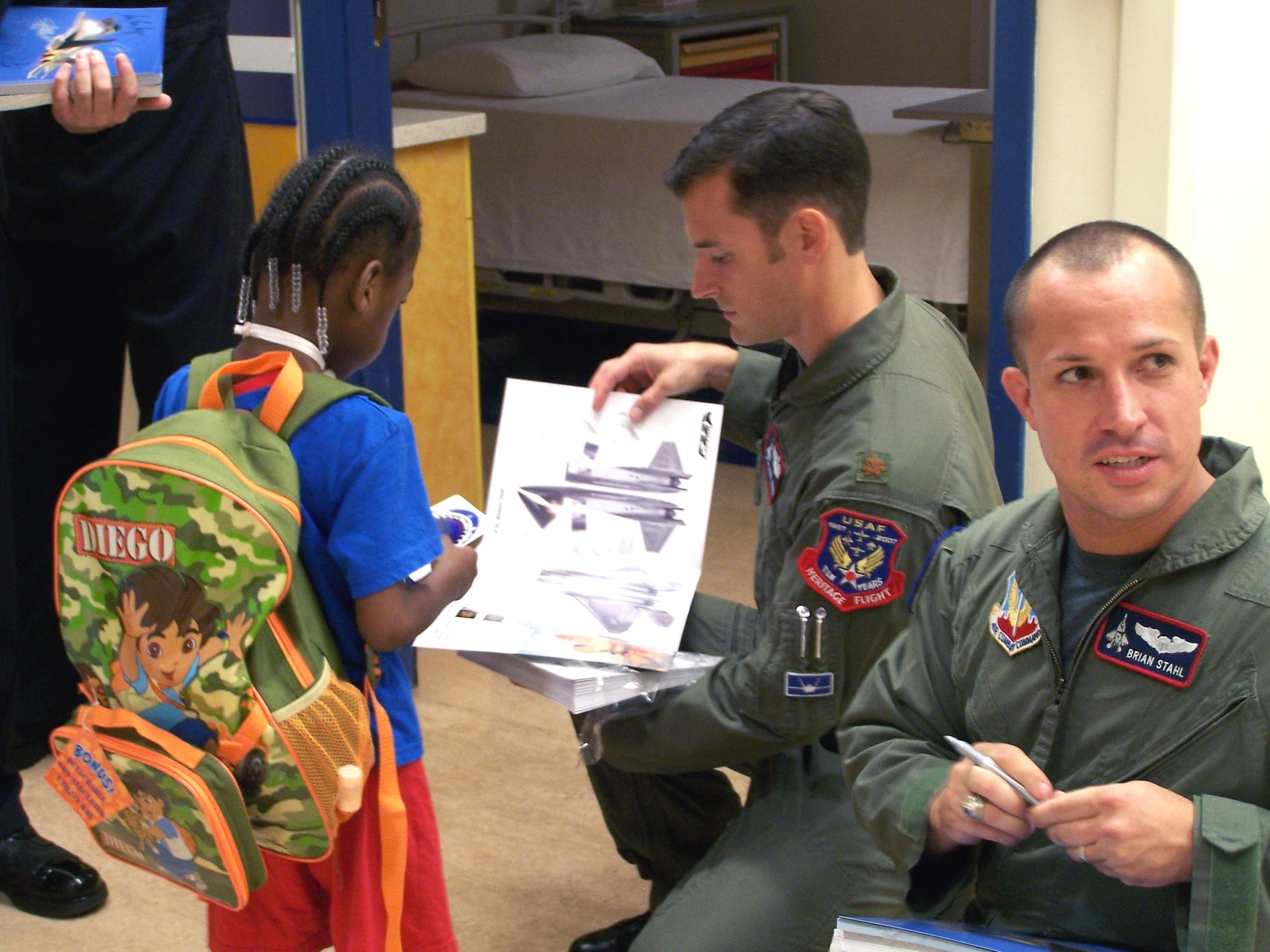 Maj. Paul Moga, the Air Force's sole F-22 Raptor demonstration pilot, explains how to construct paper models of the Raptor, while F-22 safety observer, Capt. Brian Stahl, signed autographs for patients at La Rabida Children's Hospital in Chicago Aug. 15. (U.S. Air Force photo/Capt. Rob Lazaro) 

